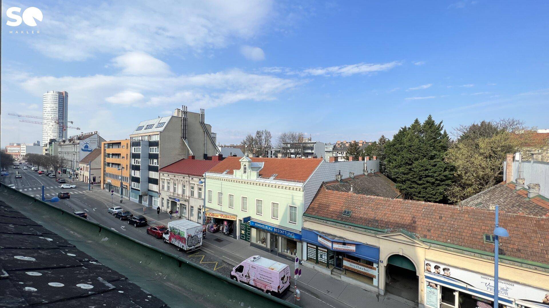 Weitblick über die Stadt mit einer Straße, Gebäuden und einem Hochhaus am Horizont.