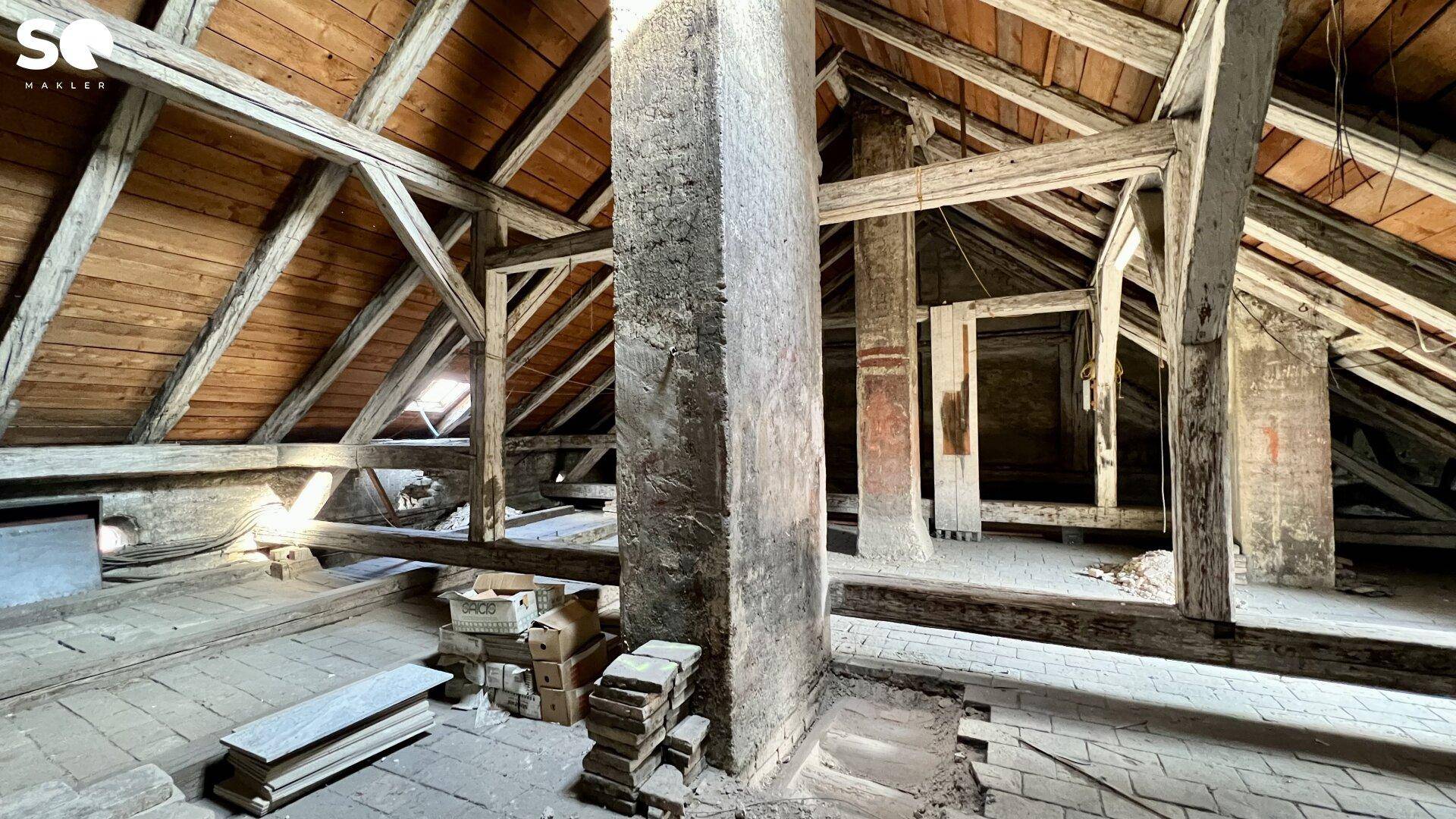 Heller Dachboden mit freiliegenden Holzbalken und einem zentralen Kamin, ideal für Umbau.