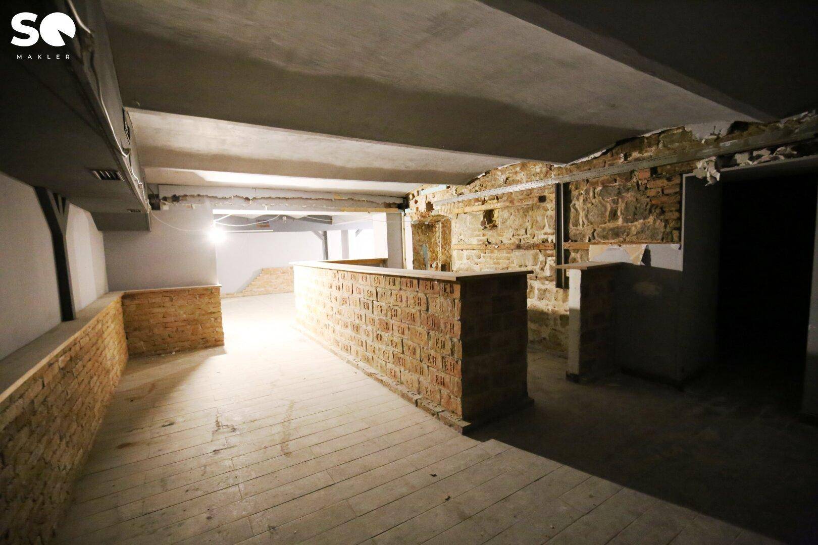 Geräumiger, unfertiger Raum mit Holzdielenboden und einer langen gemauerten Trennwand.