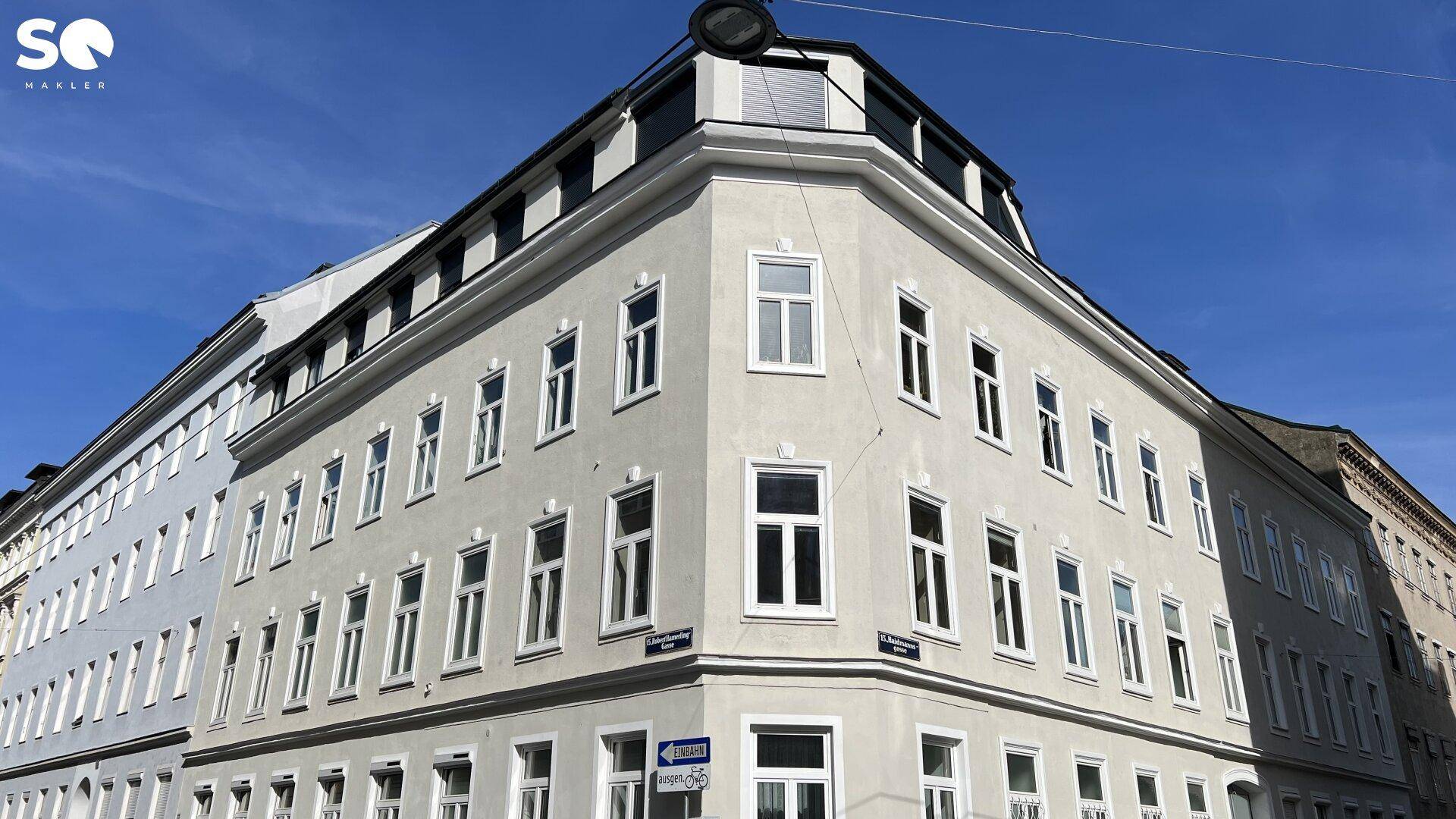 Historisches Eckgebäude mit vielen Fenstern und klassischer Architektur unter blauem Himmel.