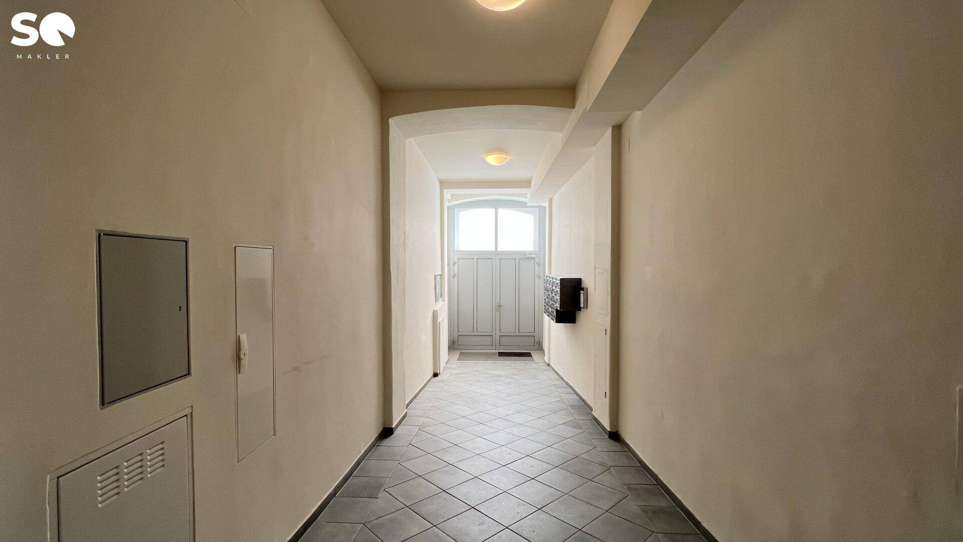 Langer, heller Flur mit Fliesenboden und Zugang zum Eingangsbereich des Gebäudes.