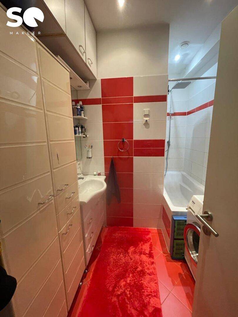 Funktionales Badezimmer mit roten und weißen Fliesen, Badewanne mit Duschfunktion und Waschmaschine.