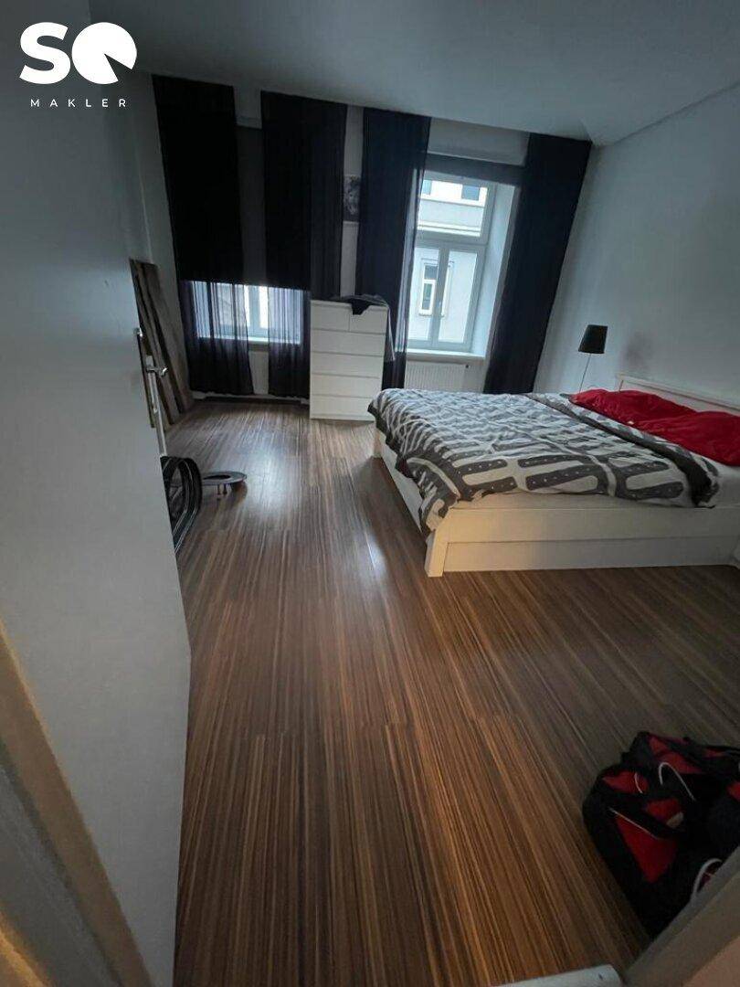 Helles Schlafzimmer mit Doppelbett, Holzboden und Blick auf die Straße durch die Fenster.