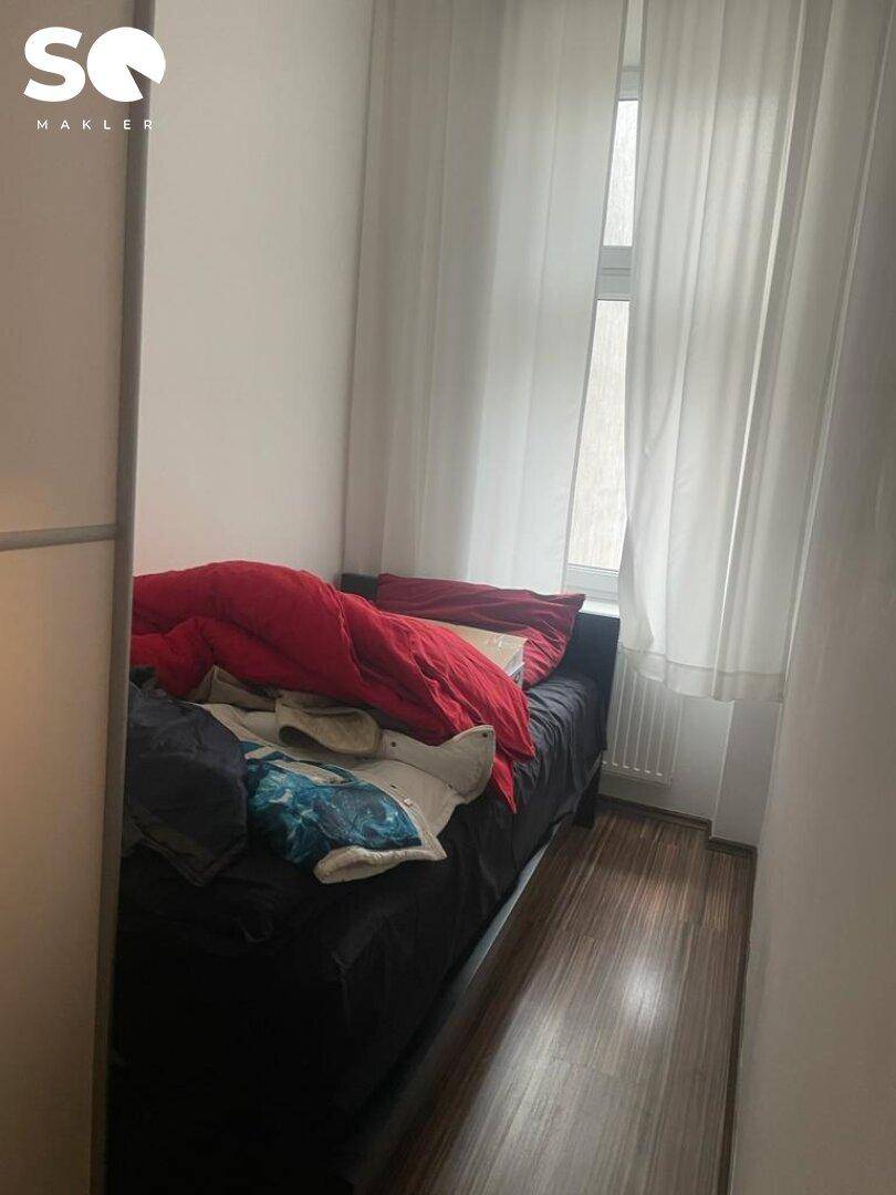 Kleines Schlafzimmer oder Gästezimmer mit Einzelbett, Holzboden und Fenster mit Vorhängen.