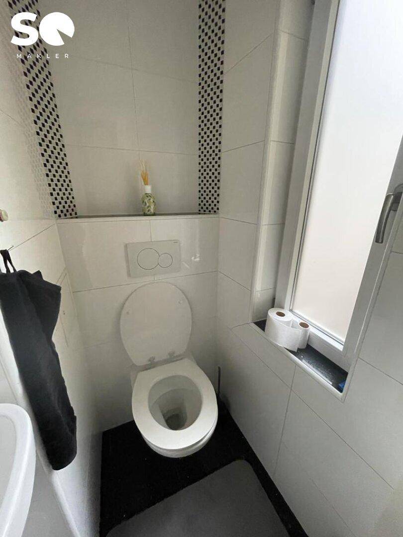 Kleines Gäste-WC mit wandhängender Toilette, kleinem Waschbecken und Fenster für Tageslicht.