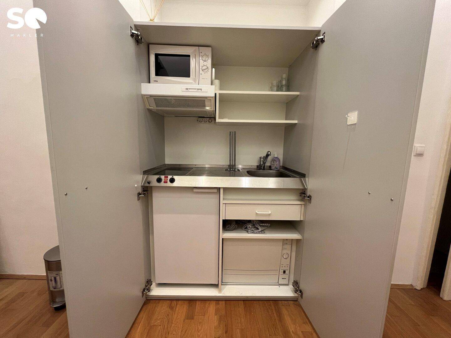 Kompakte Küchenzeile in einem Schrank integriert, ausgestattet mit Mikrowelle, Kochfeld und Kühlschrank.