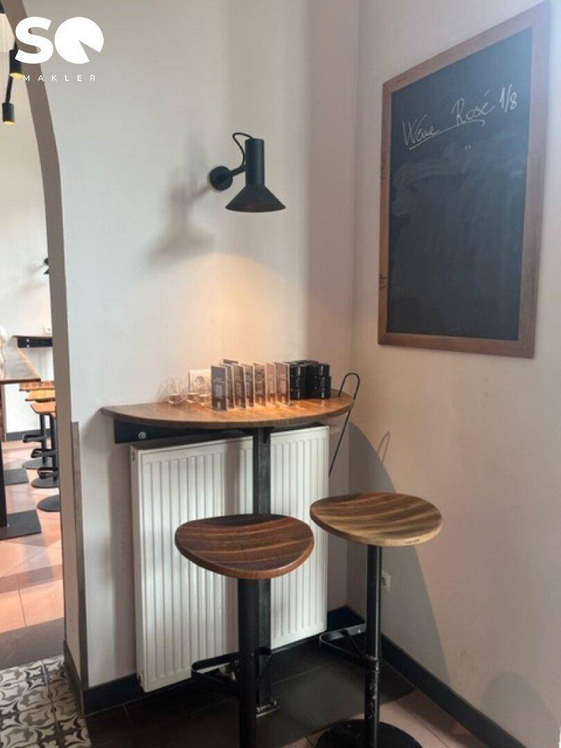 Gemütliche Ecke mit Stehtisch, Hockern, Heizkörper und einer Kreidetafel für Angebote.