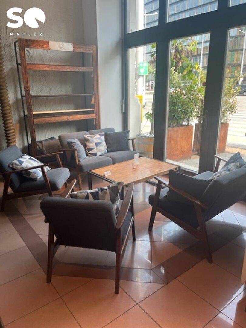 Entspannter Loungebereich mit modernen Sesseln und einem Holztisch neben den großen Fenstern.