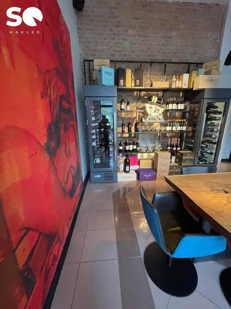 Weinregale und Kühlschränke präsentieren eine Auswahl an Weinen, akzentuiert durch eine große rote Wandkunst und Ziegelwände.