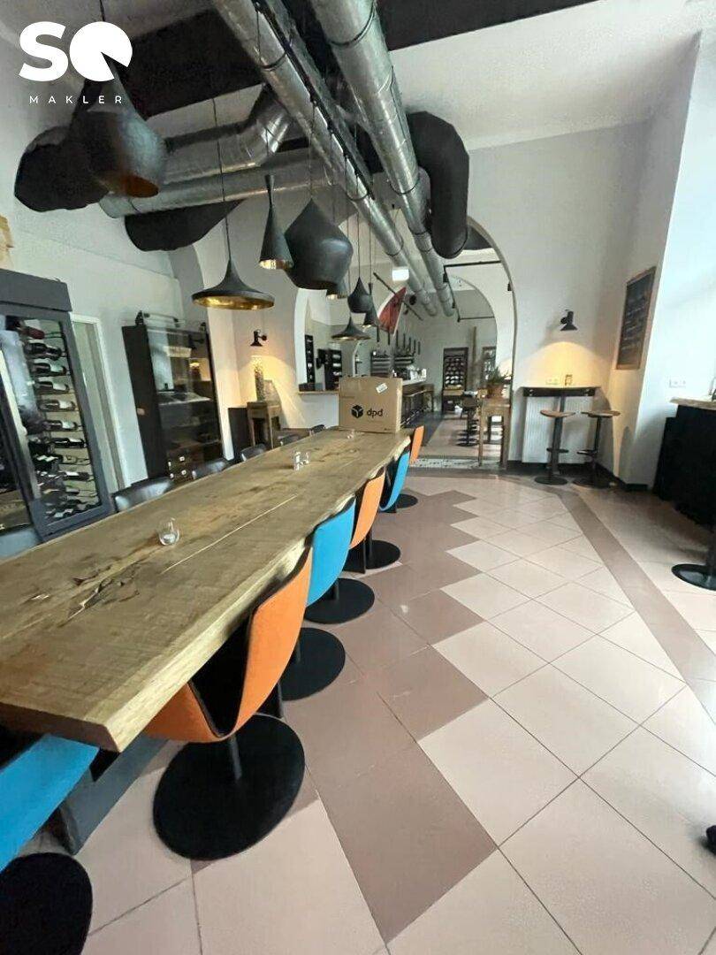 Langer Holztisch mit bunten Stühlen in einem geräumigen Bereich mit gemustertem Fliesenboden.