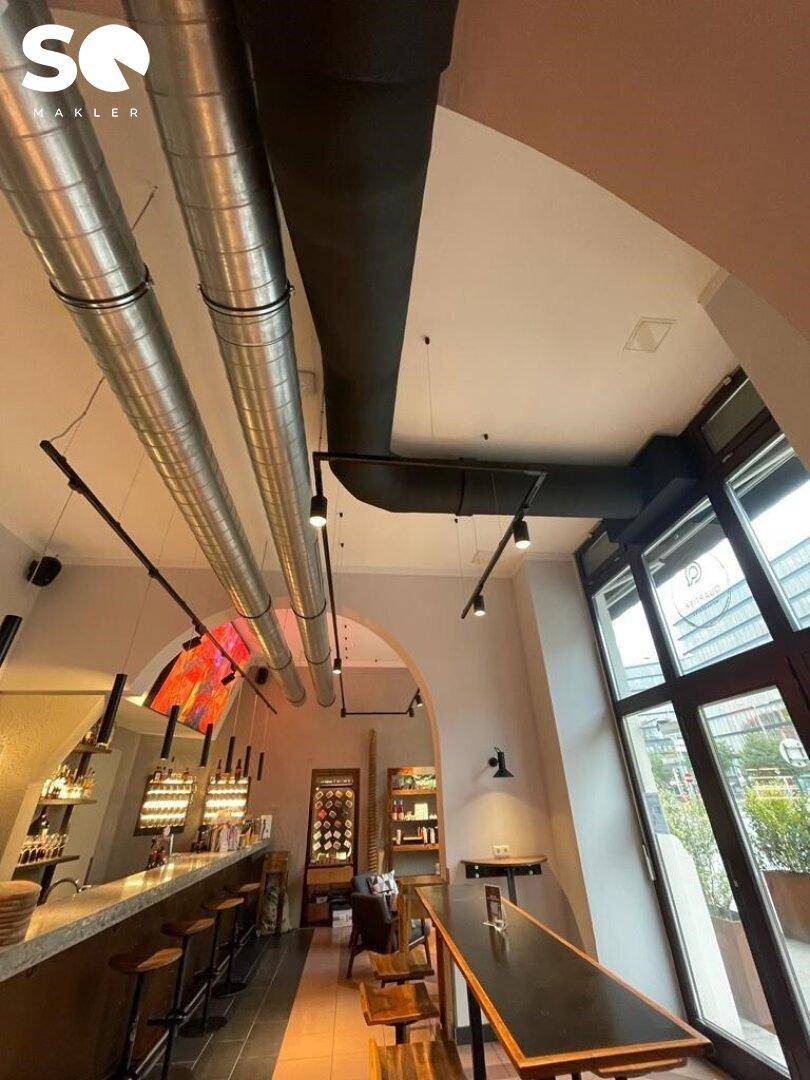 Innenansicht mit hohen Decken, sichtbaren Lüftungsrohren und großen Fenstern für viel Helligkeit.