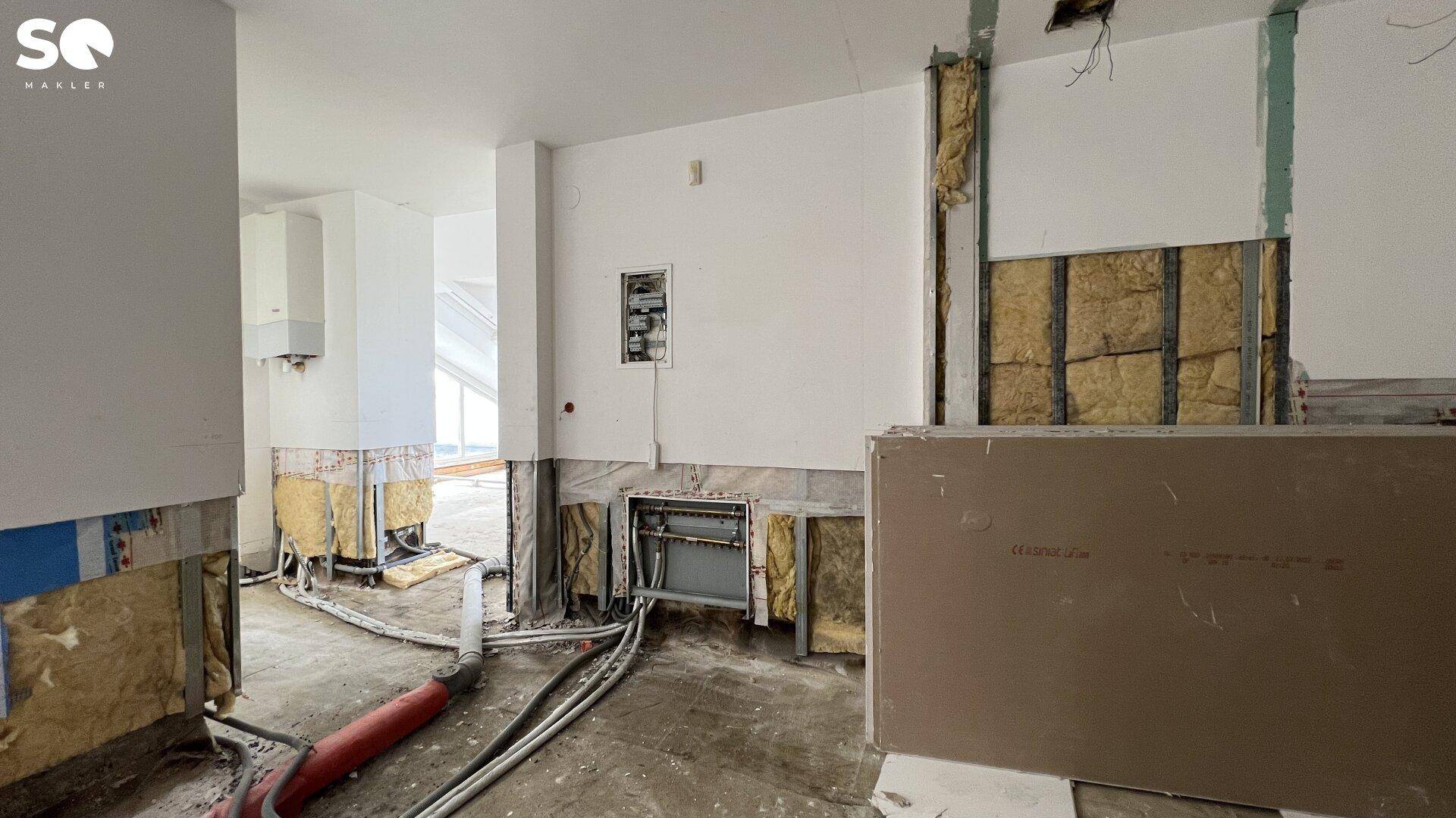 Bereich im Innenraum während der Renovierung mit sichtbaren Installationen und einem Heizkessel.