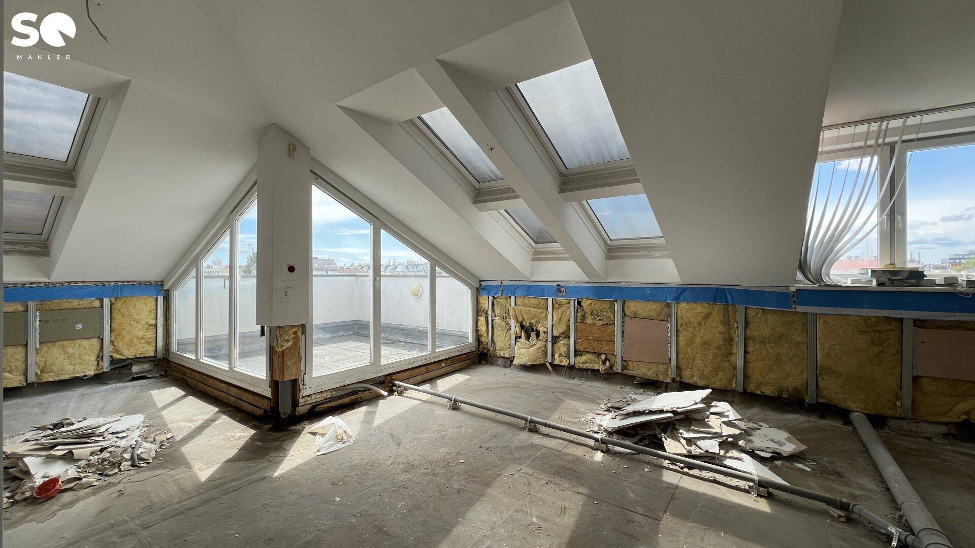 Innenraum im Dachgeschoss während der Renovierung mit vielen Dachfenstern und Zugang zu einer Terrasse.