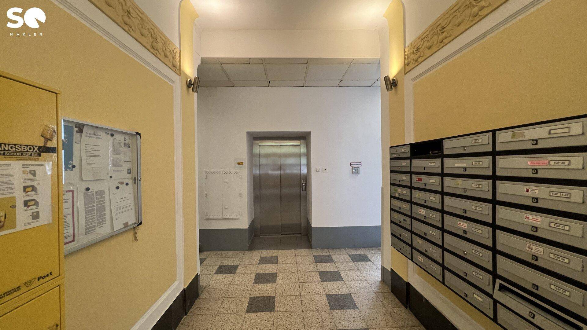 Flur im Eingangsbereich mit Briefkästen, Aufzug und gemustertem Fliesenboden.