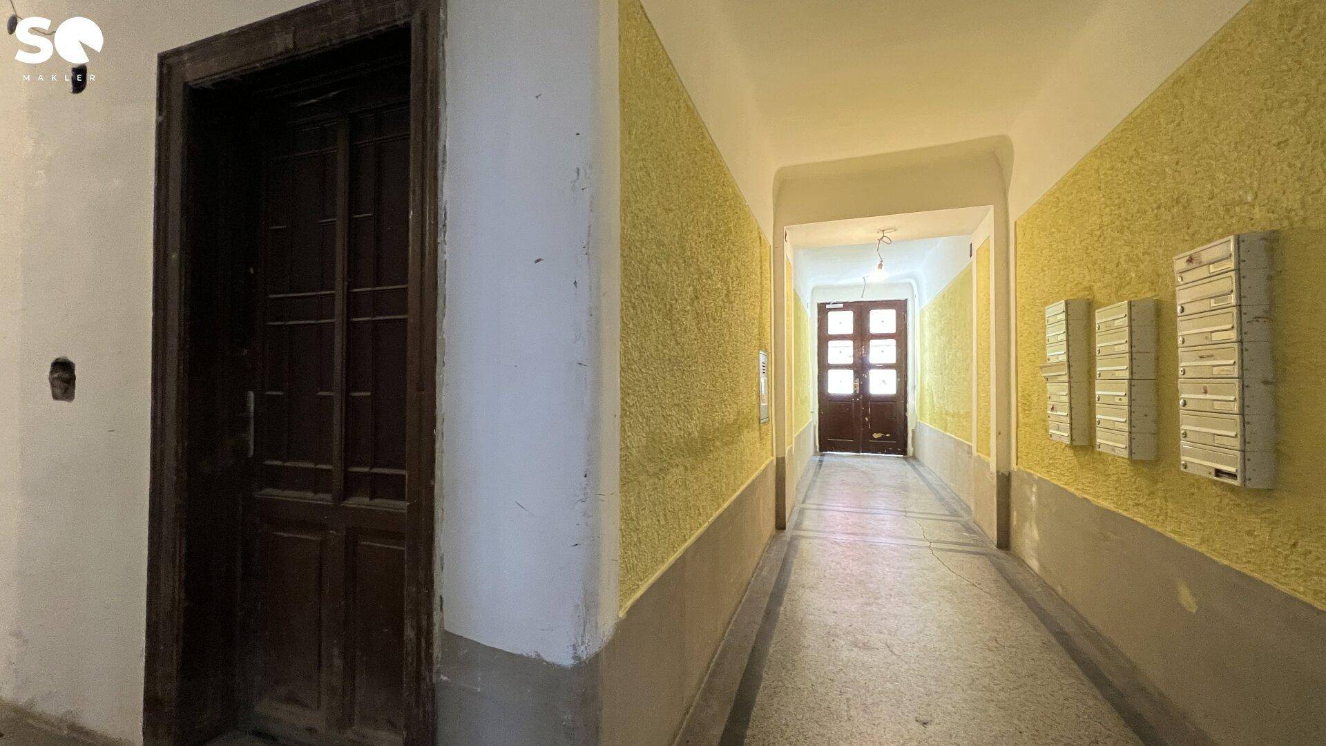 Langer Flur im Altbau mit gelb gestrichenen Wänden, Briefkästen und Holztüren.