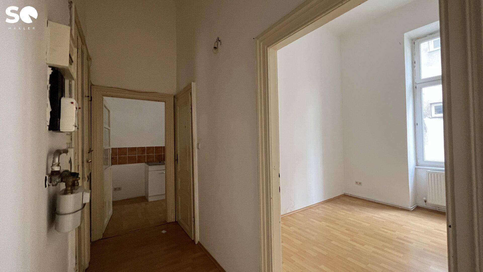 Flur mit Holzboden und Zugang zu verschiedenen Räumen, inklusive Blick in eine Küche.