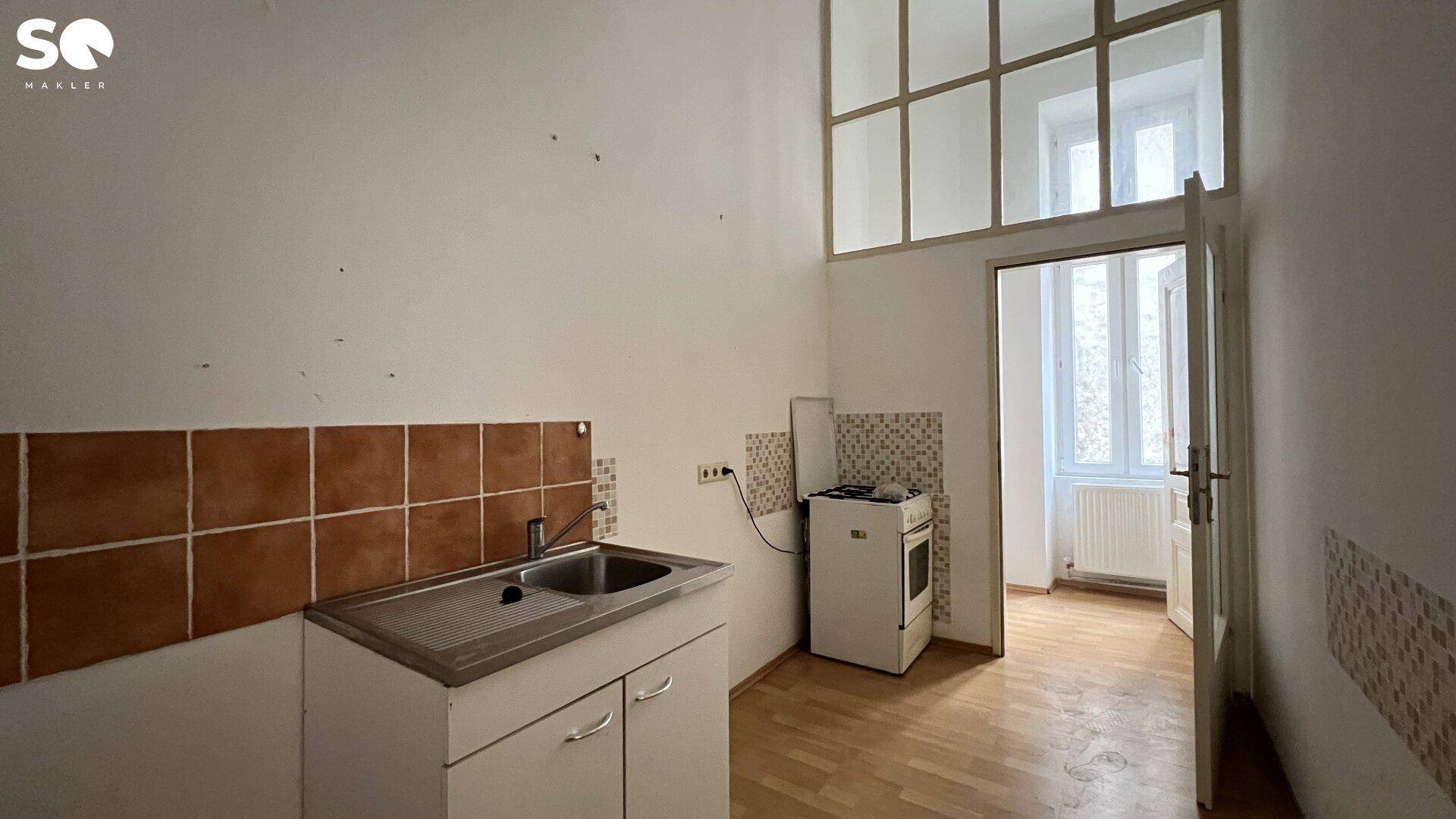 Einfache Küche mit Spüle, Herd und braunen Fliesen, bereit für eine Modernisierung.