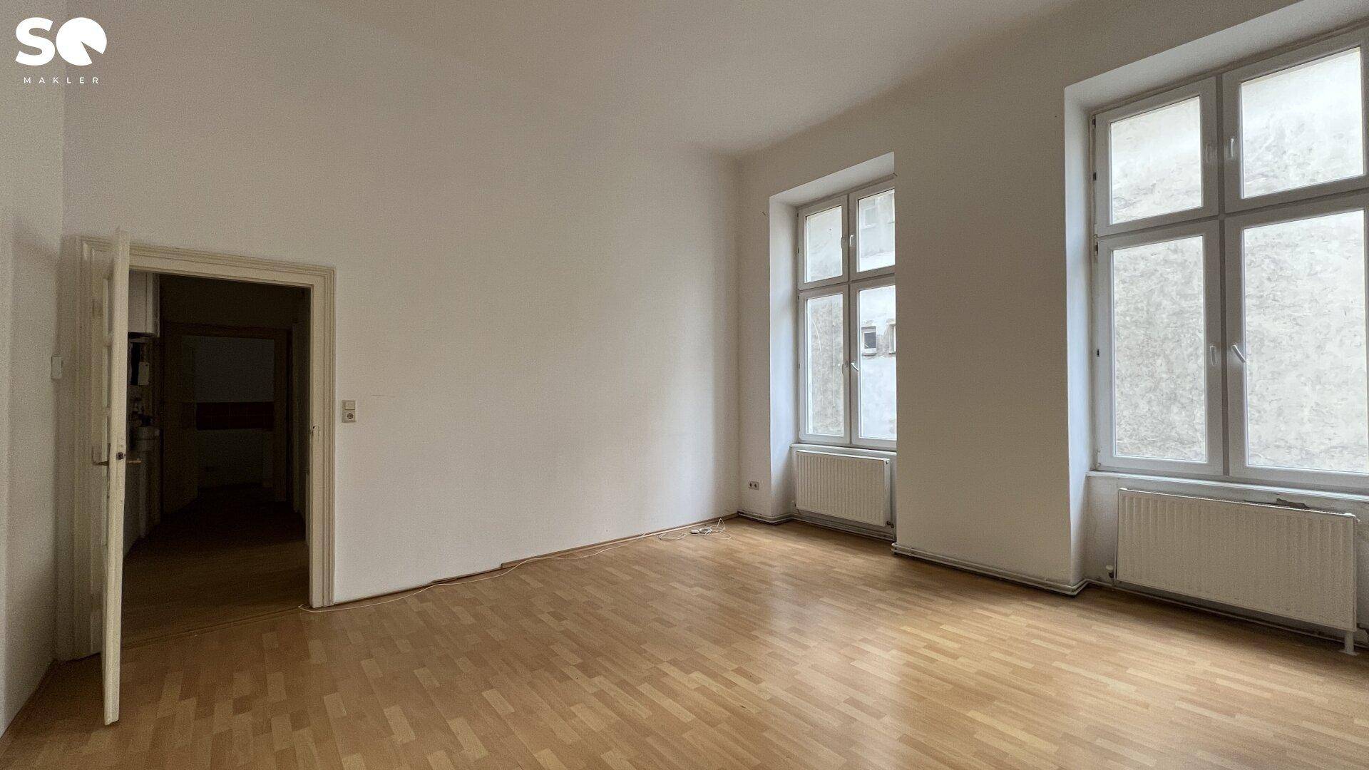 Geräumiges, leeres Wohnzimmer mit Holzboden und hohen Fenstern, ideal für individuelle Gestaltung.