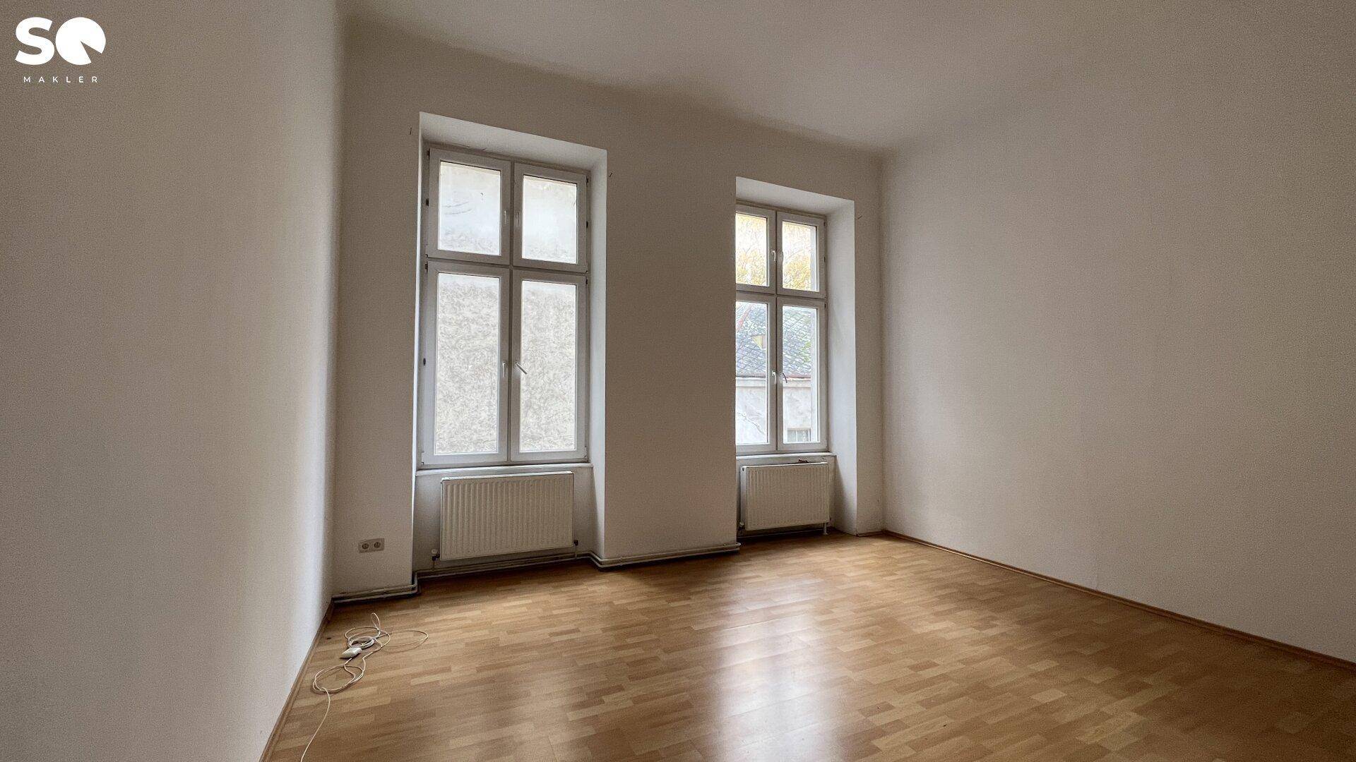 Leeres Schlafzimmer mit Holzboden und zwei hohen Fenstern, bietet viel Gestaltungspotenzial.