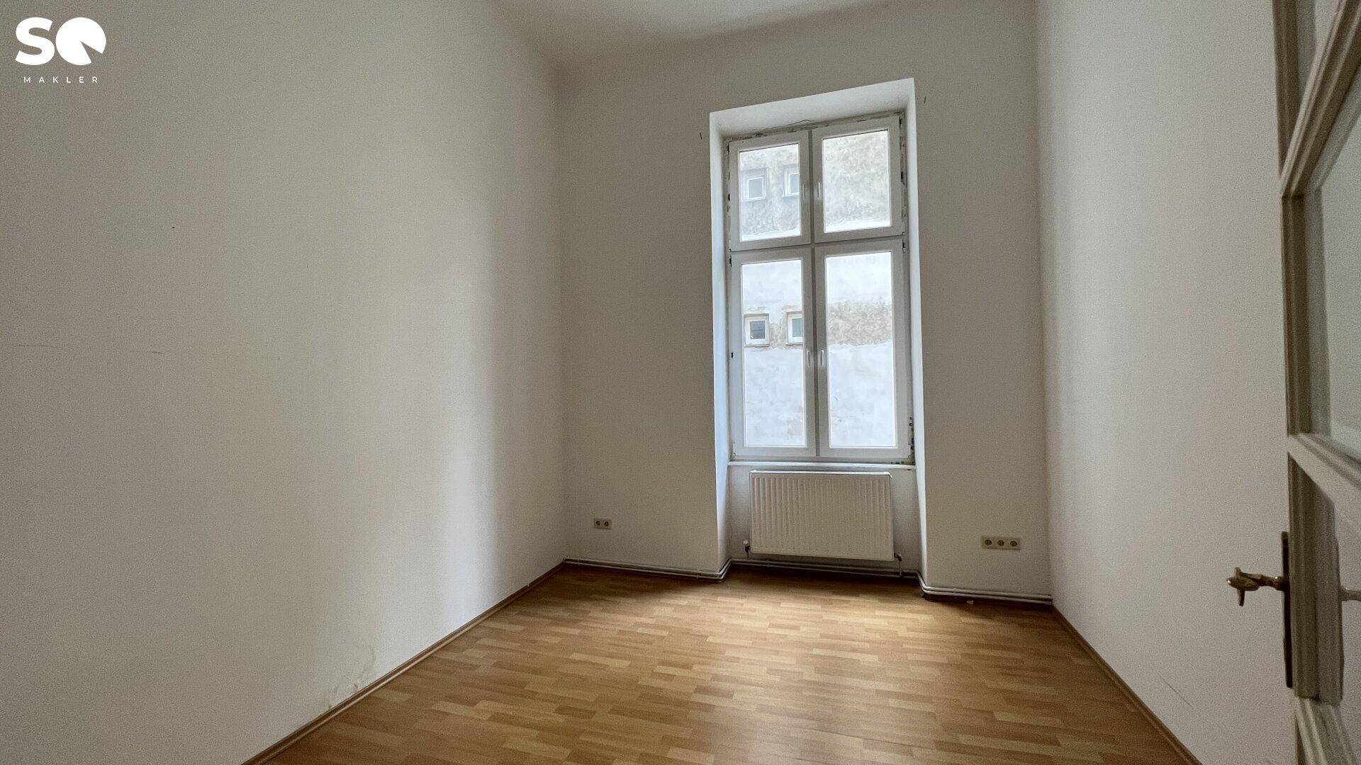 Kleines, helles Zimmer mit Holzboden und einem hohen Fenster, ideal als Kinder- oder Arbeitszimmer.