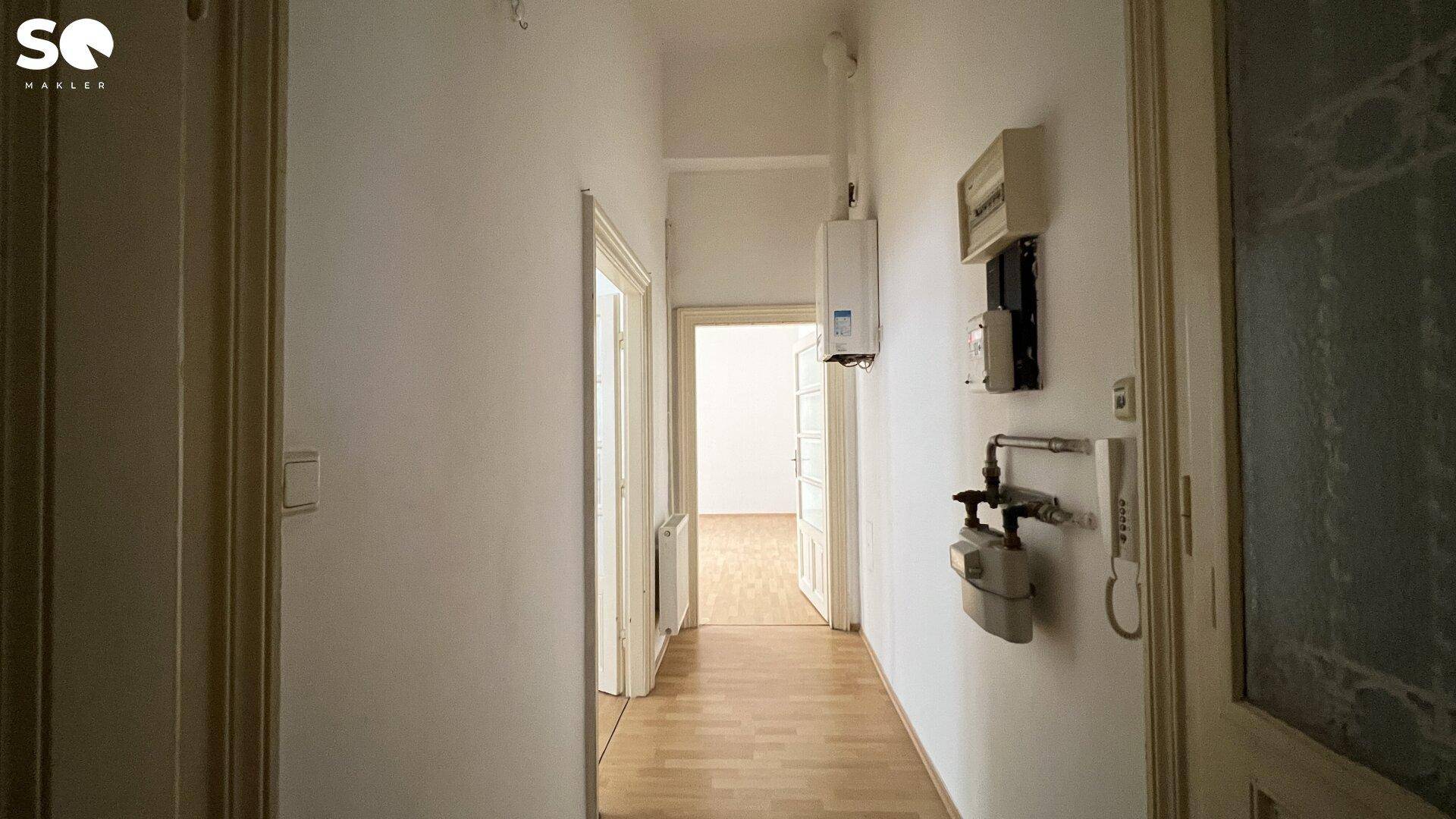 Langer Flur mit Holzboden und sichtbaren Installationen, führt zu weiteren Zimmern.