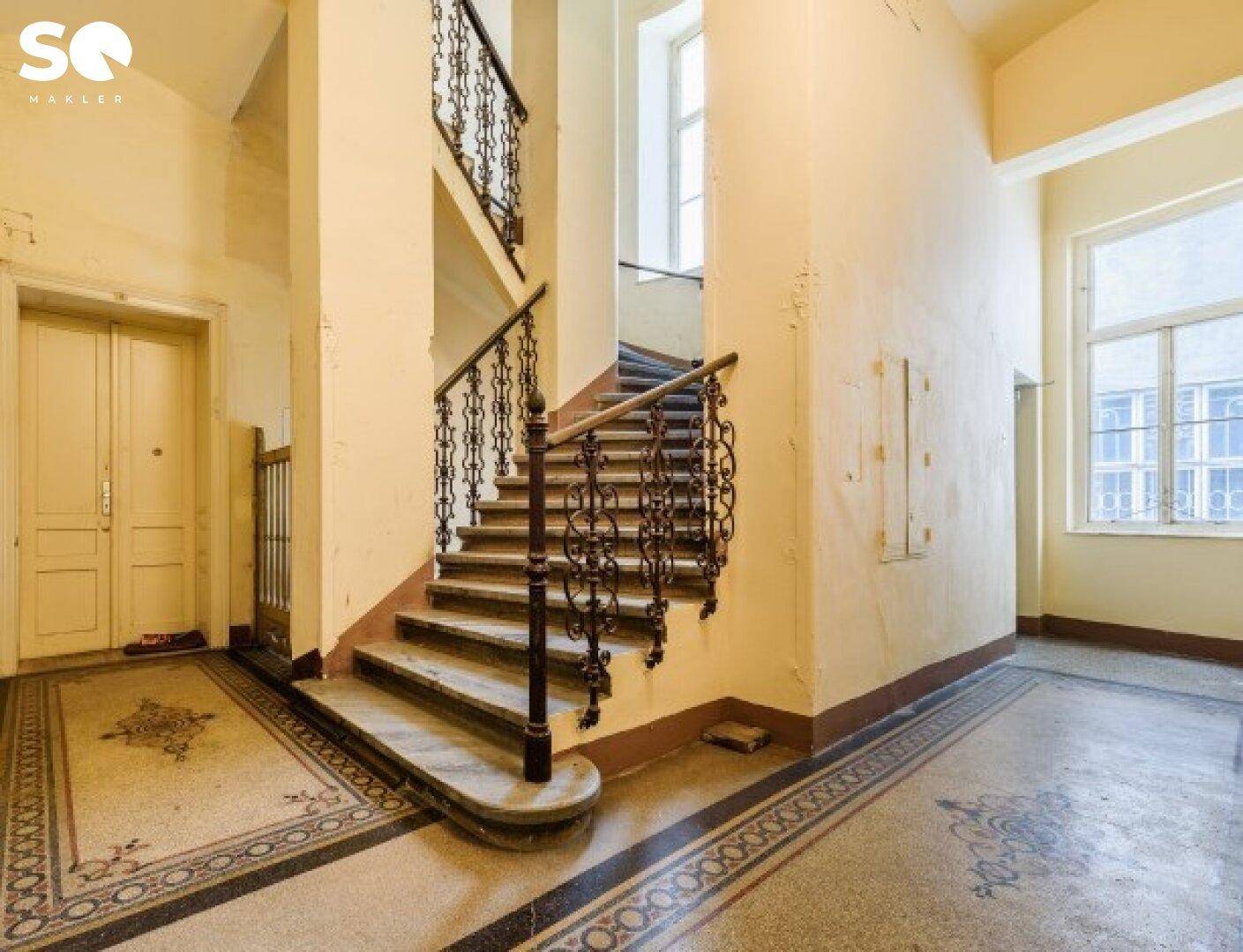 Historisches Treppenhaus mit schmiedeeisernem Geländer und gemustertem Terrazzoboden.