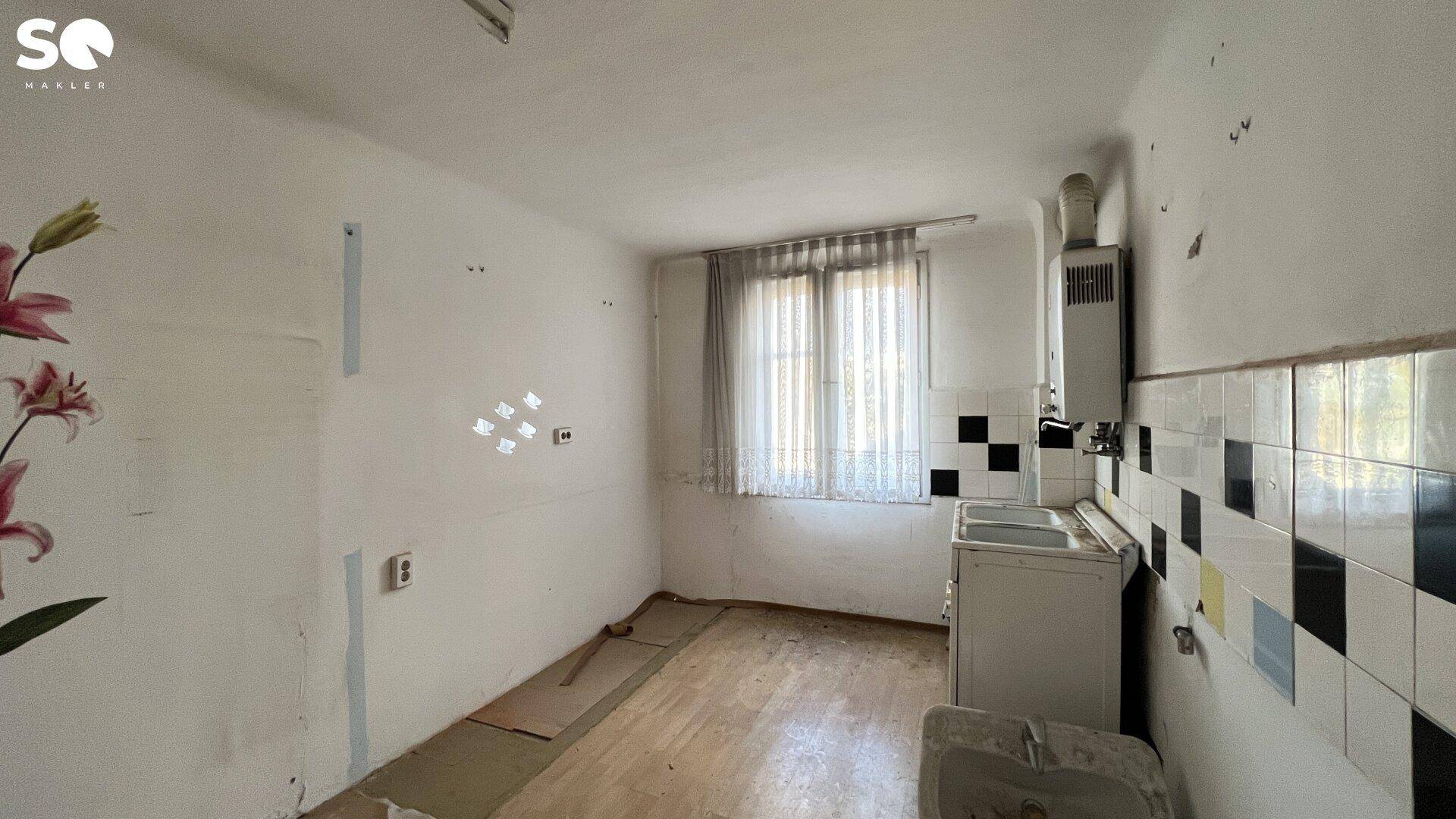 Leere Küche mit alten Fliesen, Fenster und Renovierungsbedarf.