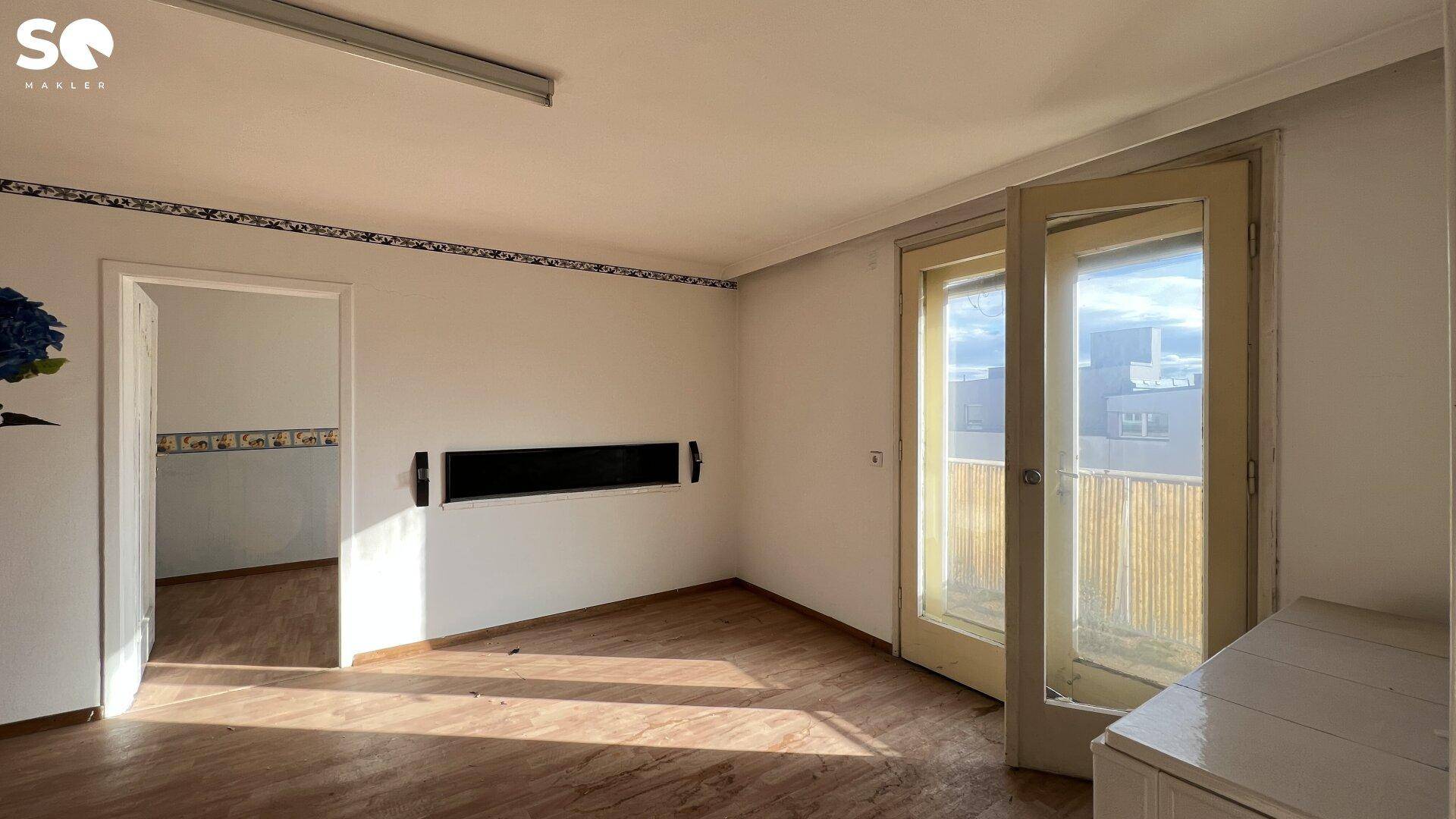 Unmöbliertes Zimmer mit Holzboden, Balkonzugang und Renovierungsbedarf.