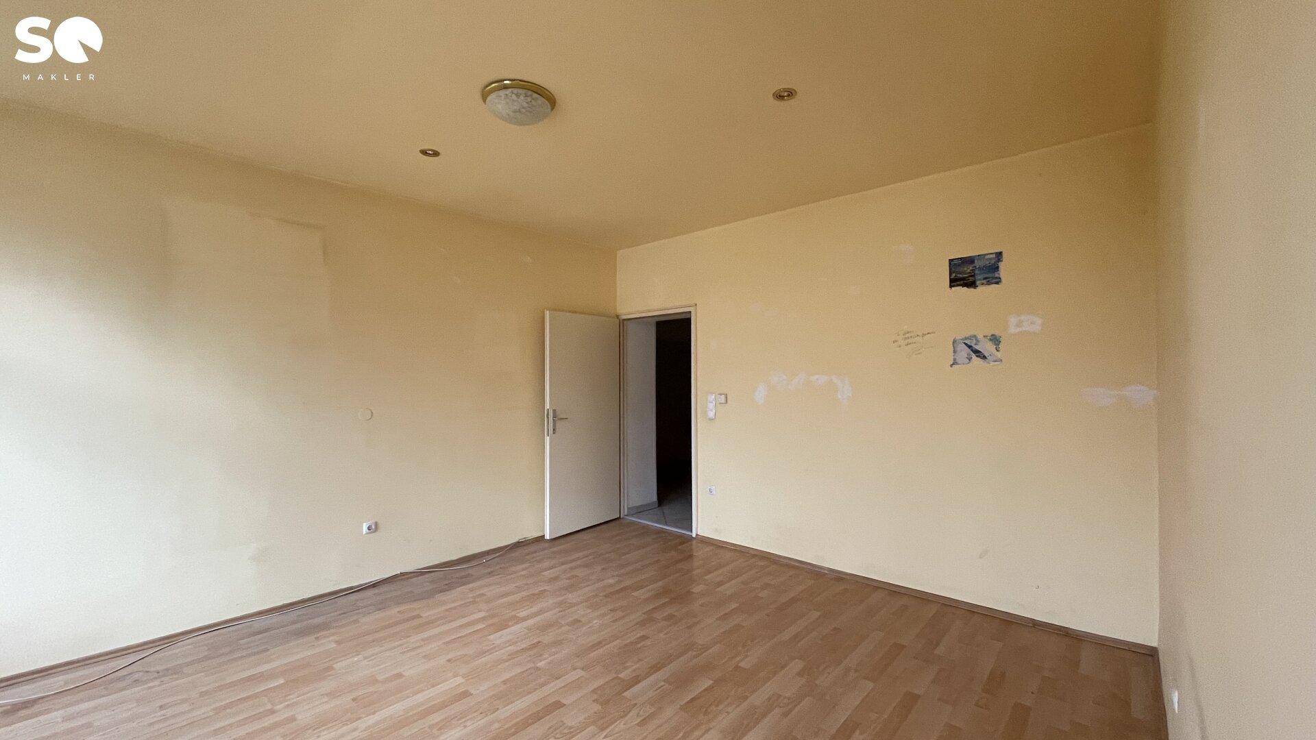 Unmöbliertes Zimmer mit gelblichen Wänden und Holzboden, bereit für neue Bewohner.