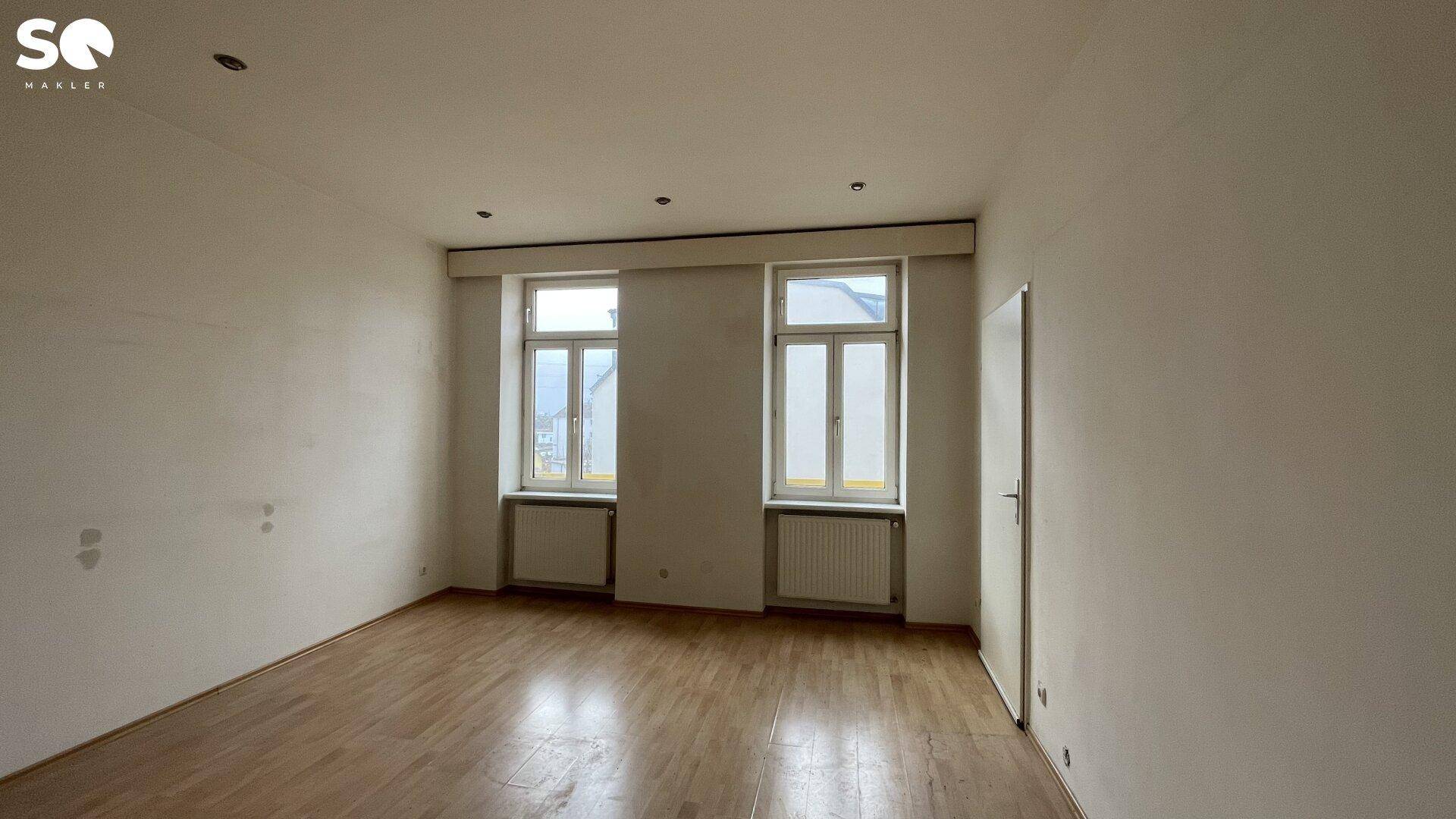 Geräumiges Zimmer mit Holzboden und viel Tageslicht durch die großen Fenster.