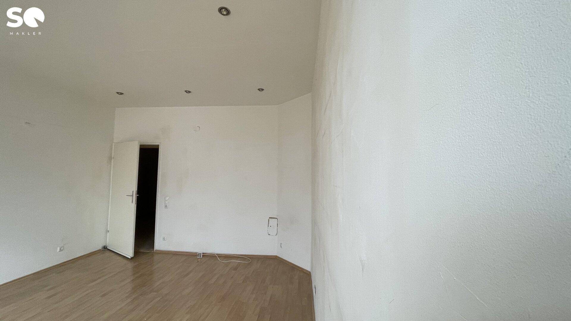 Renoviertes Zimmer mit weiß gestrichenen Wänden und glänzendem Holzfußboden.