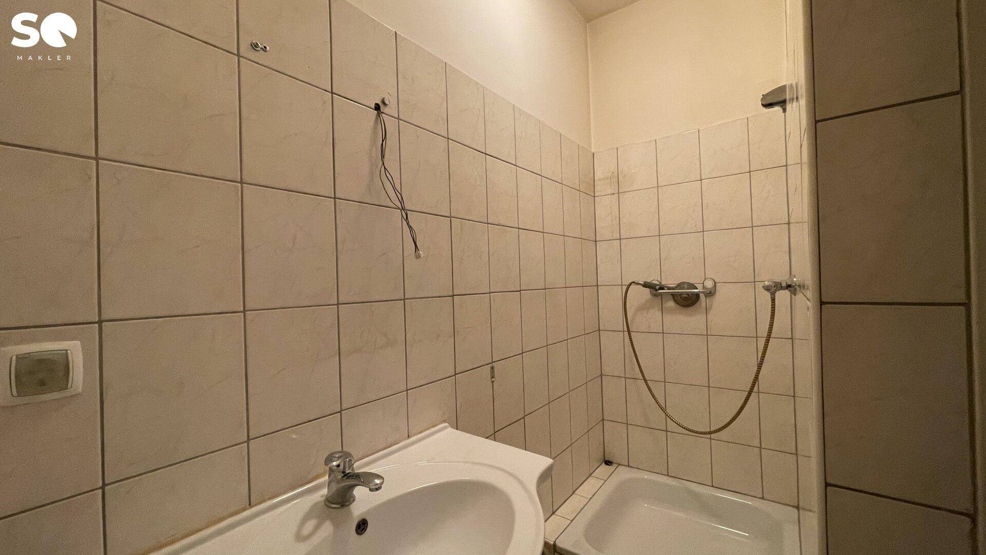 Funktionales Badezimmer mit hellen Fliesen, Waschbecken und einer Duschwanne.