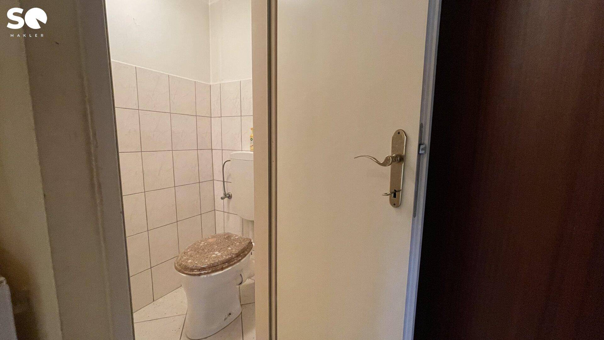 Separates WC mit gefliesten Wänden und einer einfachen Toilette.