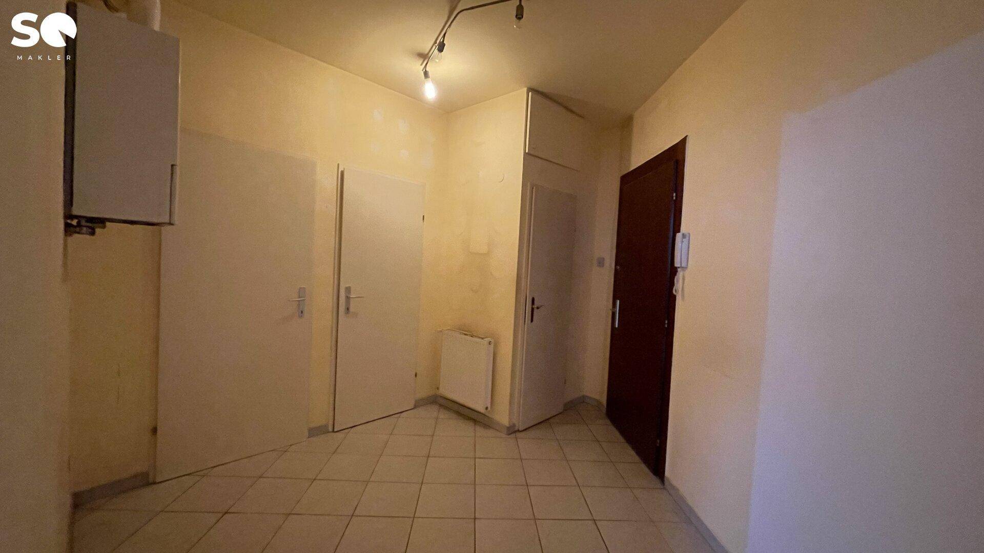 Eingangsbereich mit Fliesenboden, mehreren Türen und einem Heizkessel an der Wand.