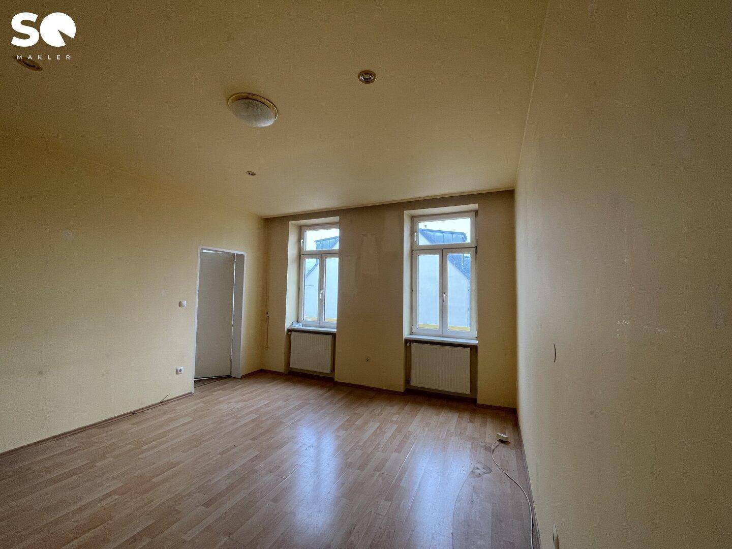 Helles Zimmer mit gelblichen Wänden, Holzboden und zwei Fenstern für viel Licht.