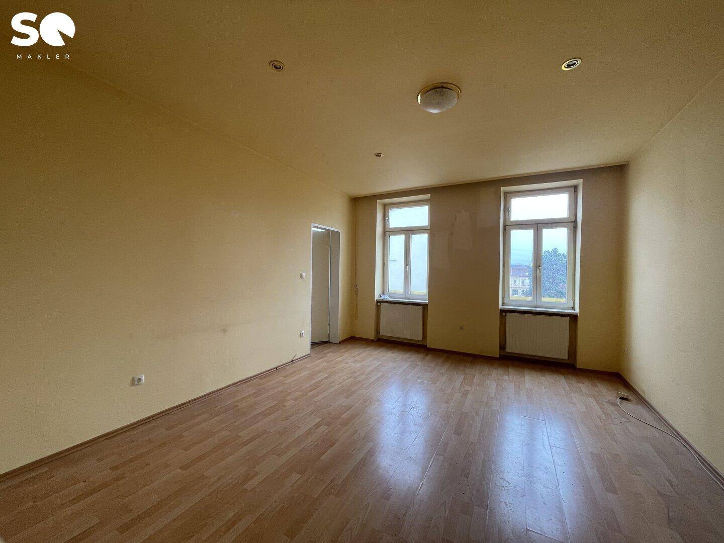 Geräumiges Zimmer mit gelblichen Wänden, Holzboden und Blick nach draußen.