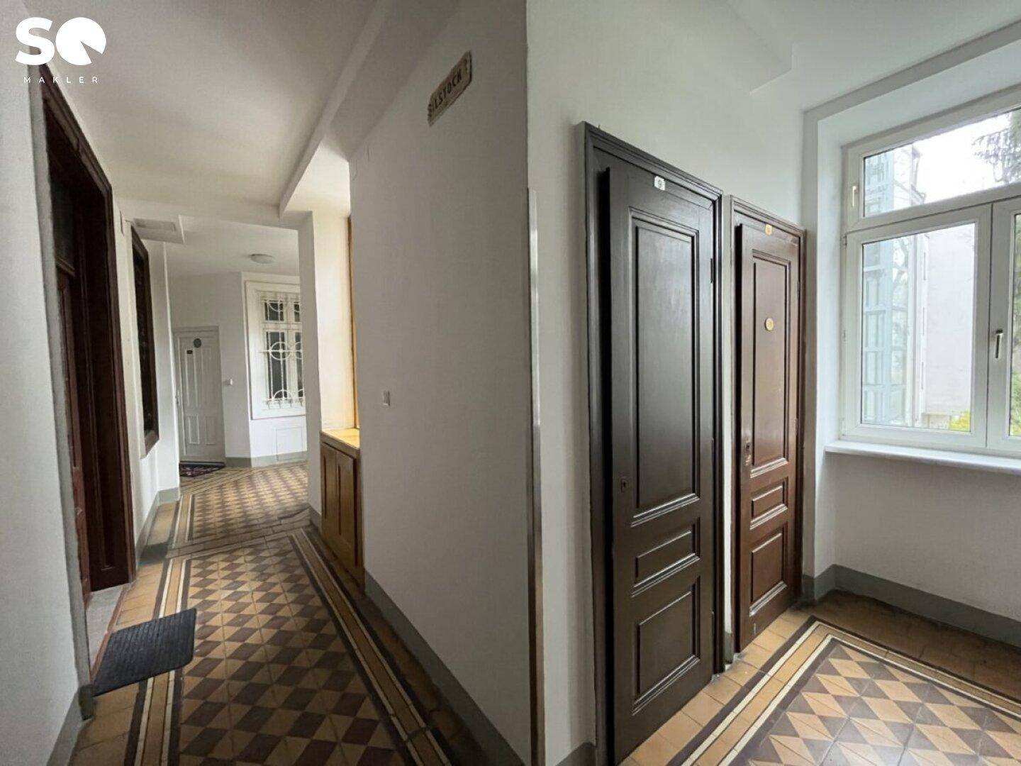 Langer Flur mit mehreren Türen, gemustertem Fliesenboden und einem großen Fenster.
