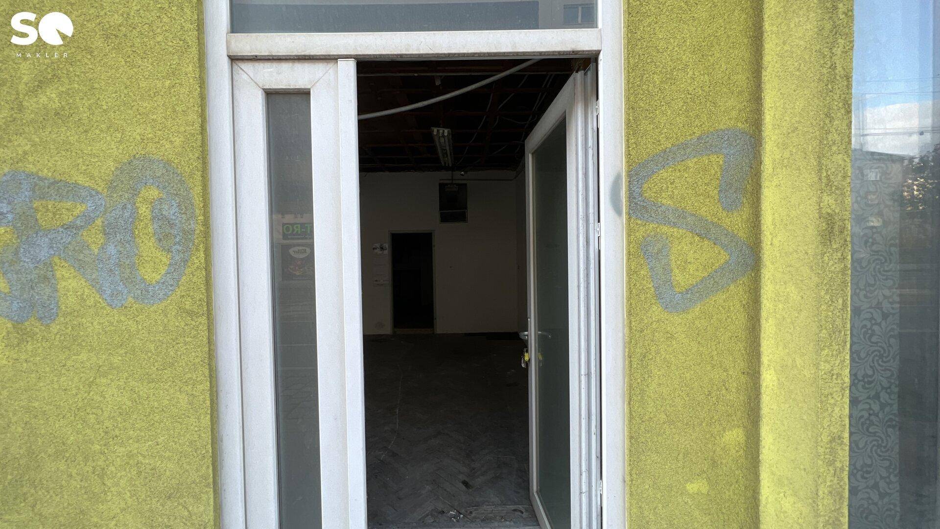 Eingangsbereich eines Gebäudes mit gelber Fassade und offener Tür zum Innenraum.