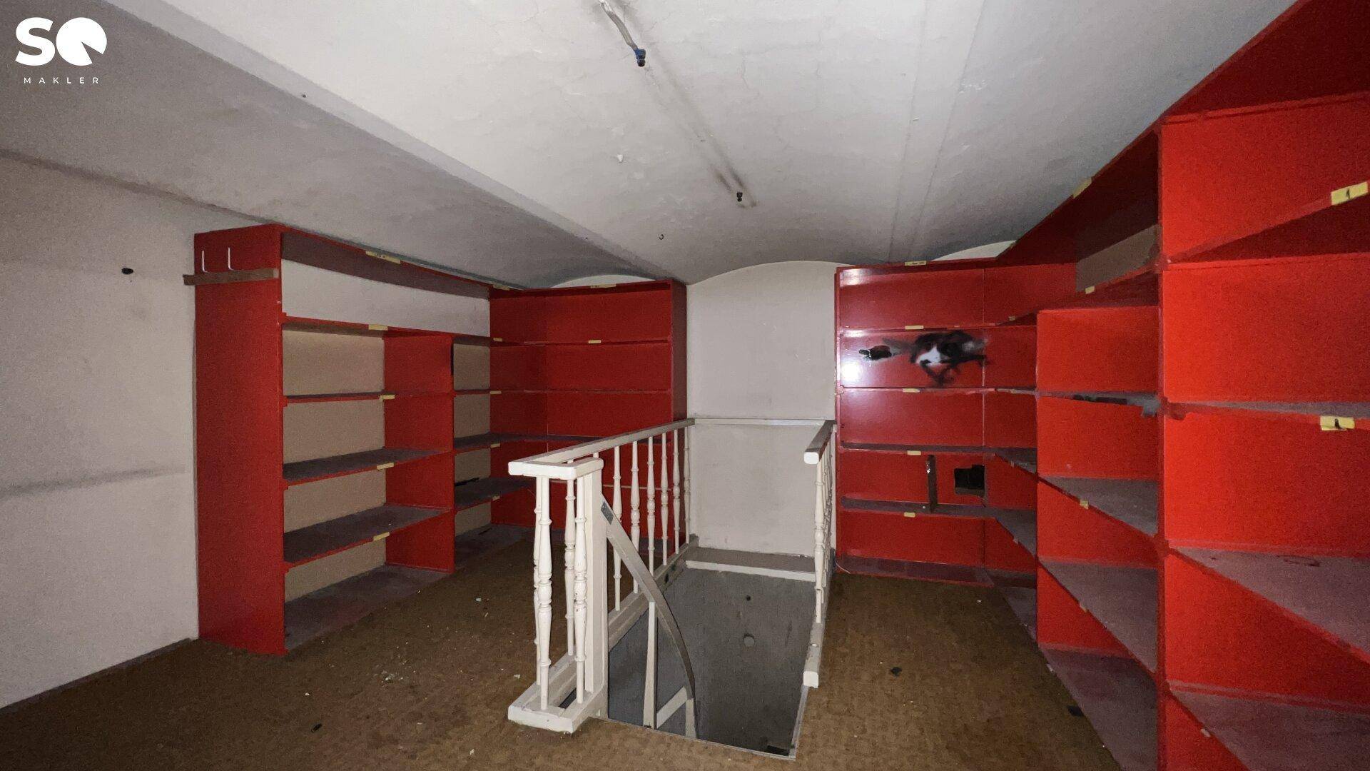 Kellerraum mit roten Regalen und Treppe, die in einen tieferen Bereich führt.