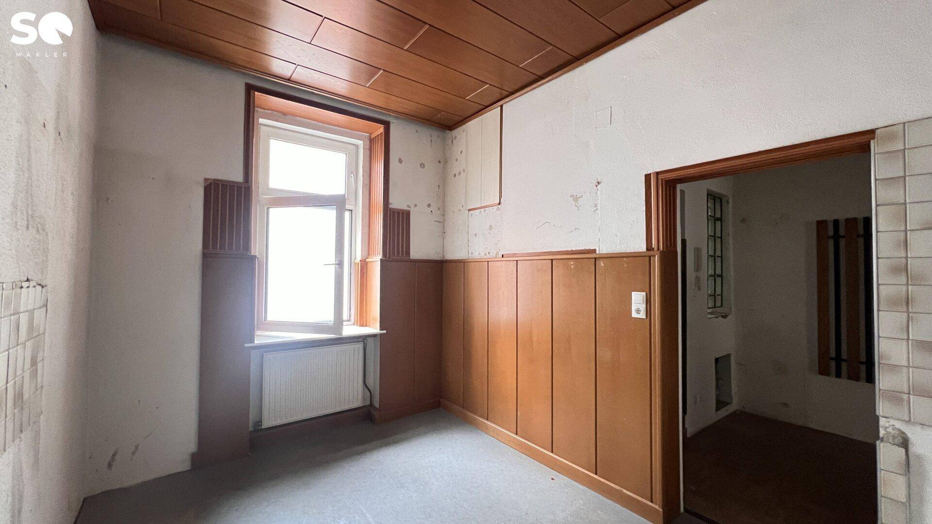Renovierungsbedürftiger Raum mit Holzvertäfelung, unverputzten Wänden und einer dunklen Kassettendecke.