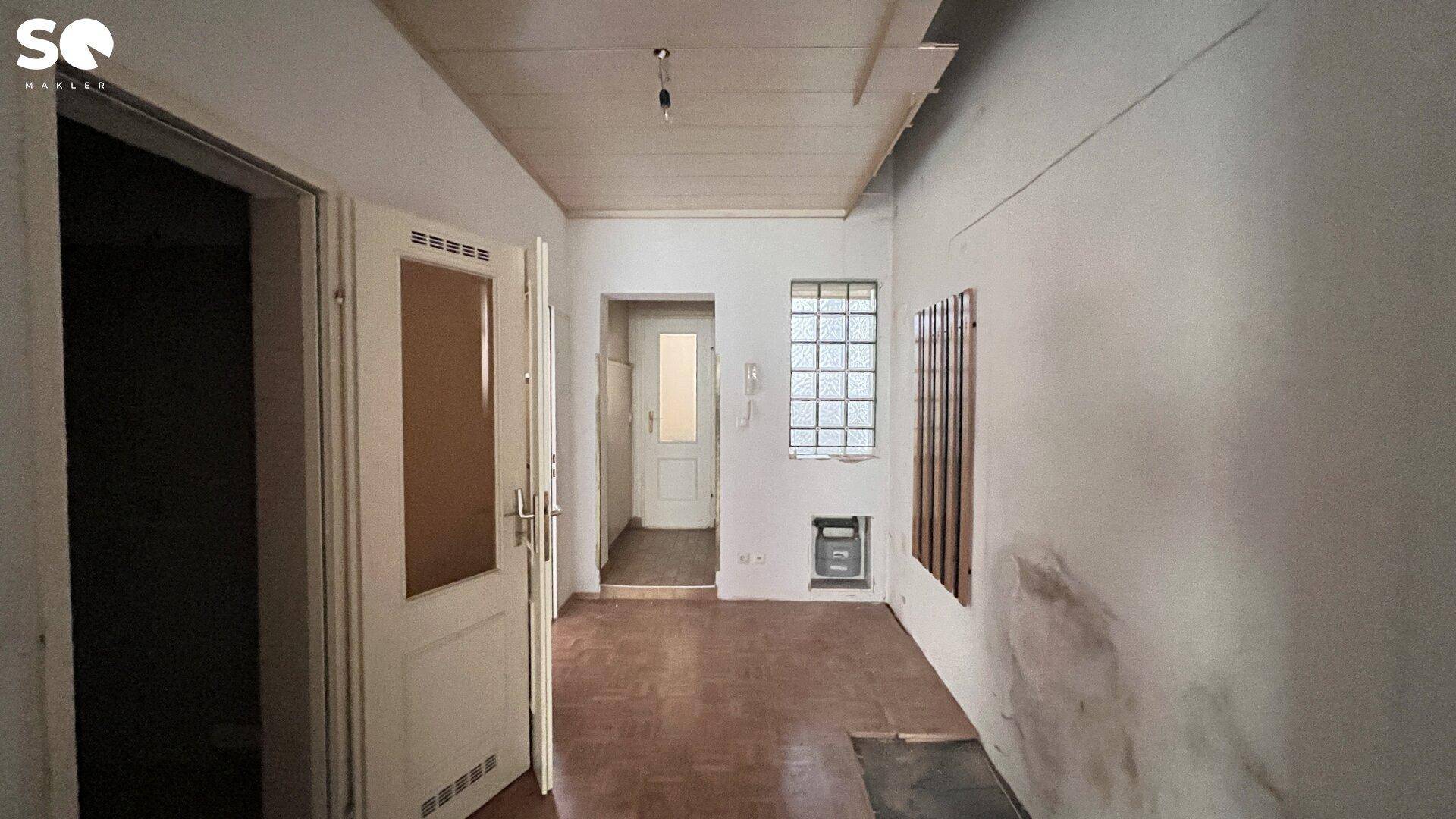 Renovierungsbedürftiger Flur mit unverputzten Wänden und einer Glasbausteinwand, die Licht hereinlässt.