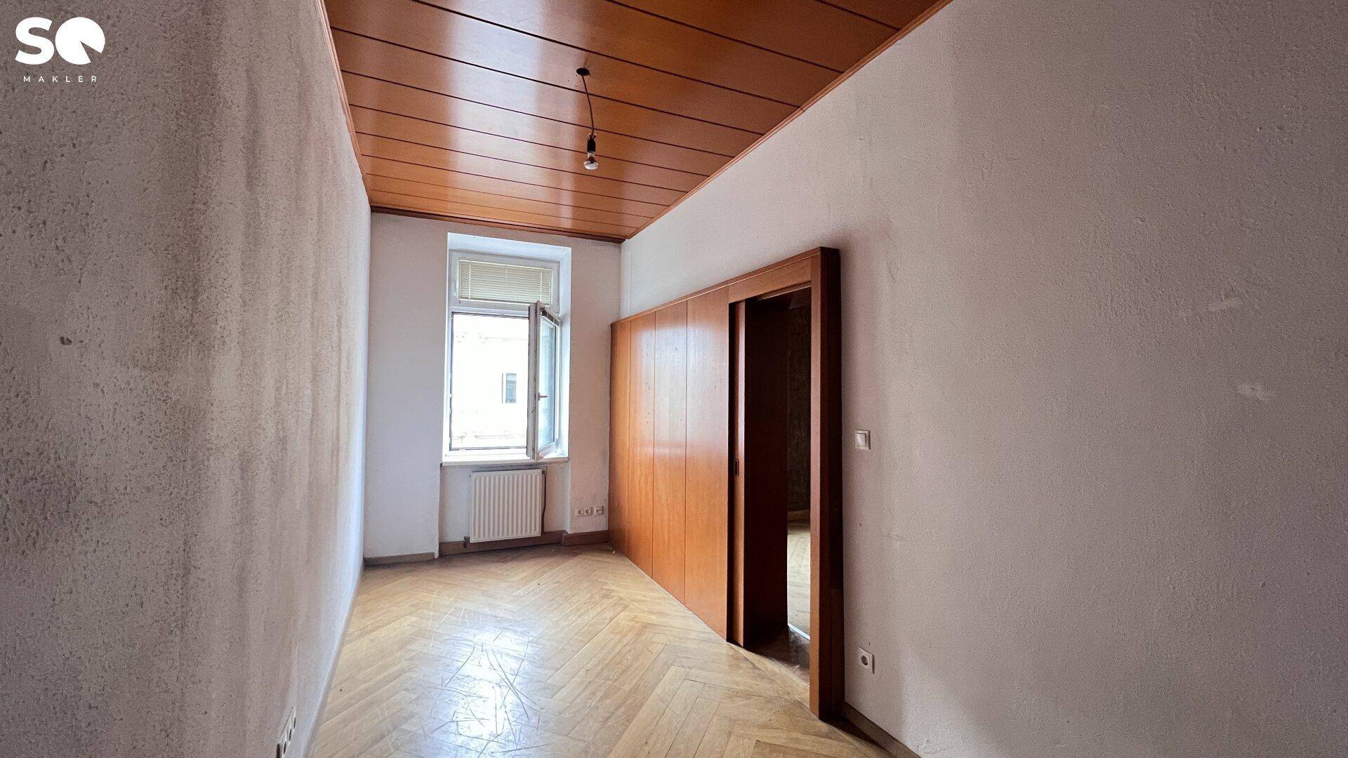 Leerer Raum mit Fischgrätparkett, Holzschiebetür und einer dunklen Kassettendecke.