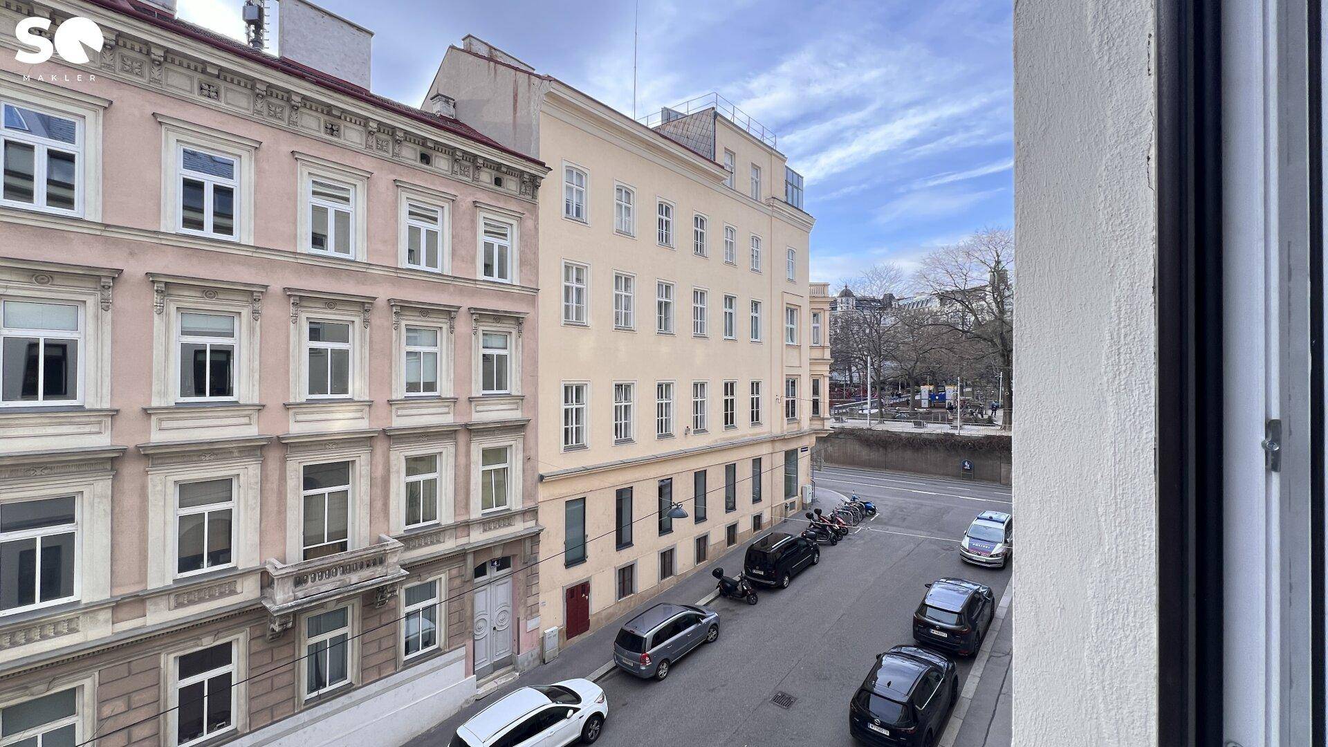Blick aus dem Fenster auf eine belebte Straße mit parkenden Autos und historischen Gebäuden.