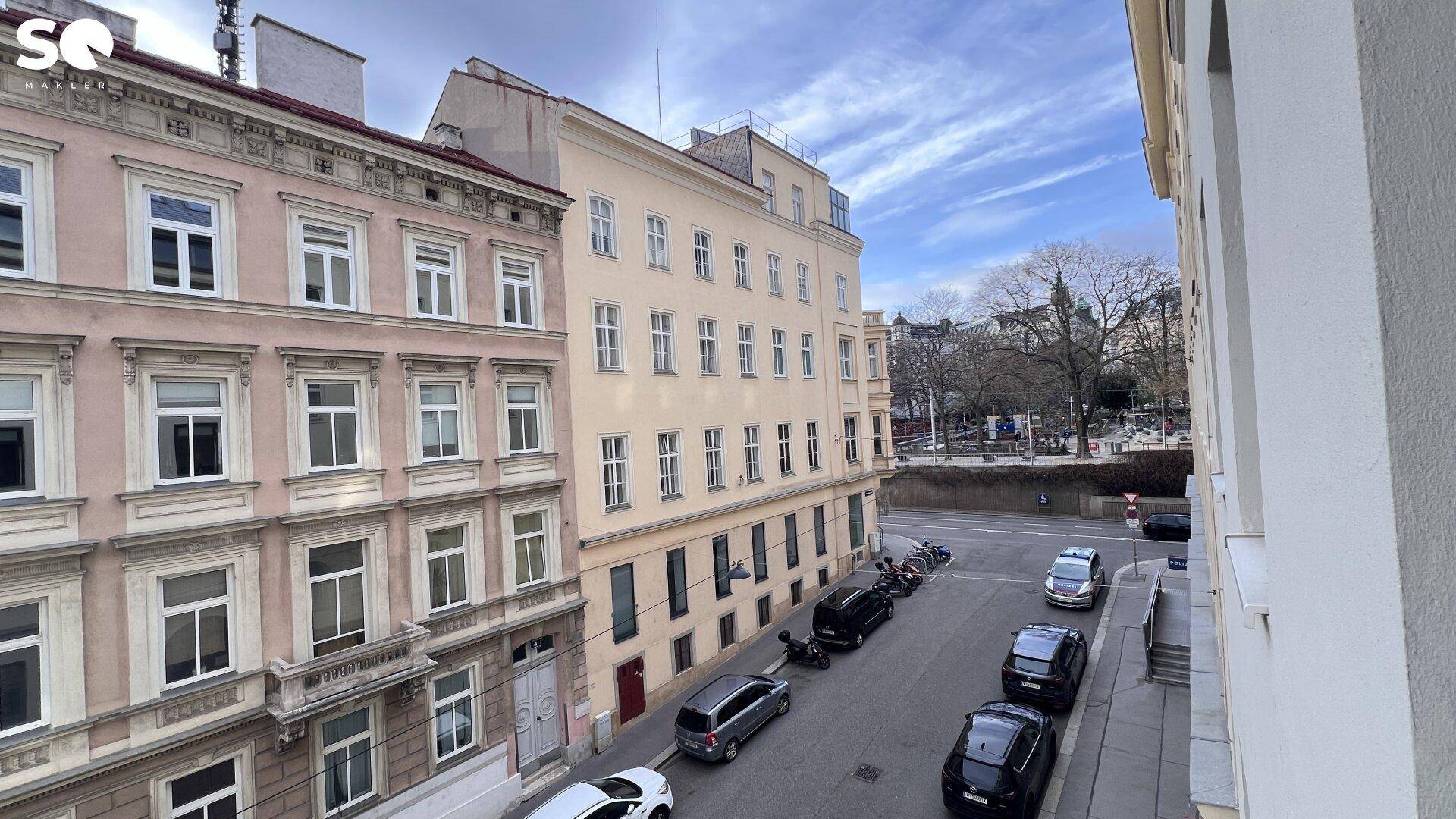 Blick aus dem Fenster auf eine belebte Straße mit parkenden Autos und historischen Gebäuden.