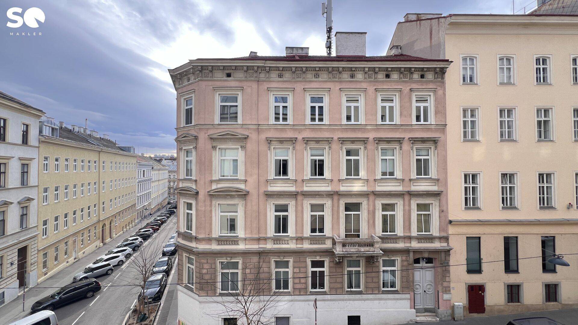 Historisches Gebäude mit rosafarbener Fassade und vielen Fenstern an einer städtischen Straße.