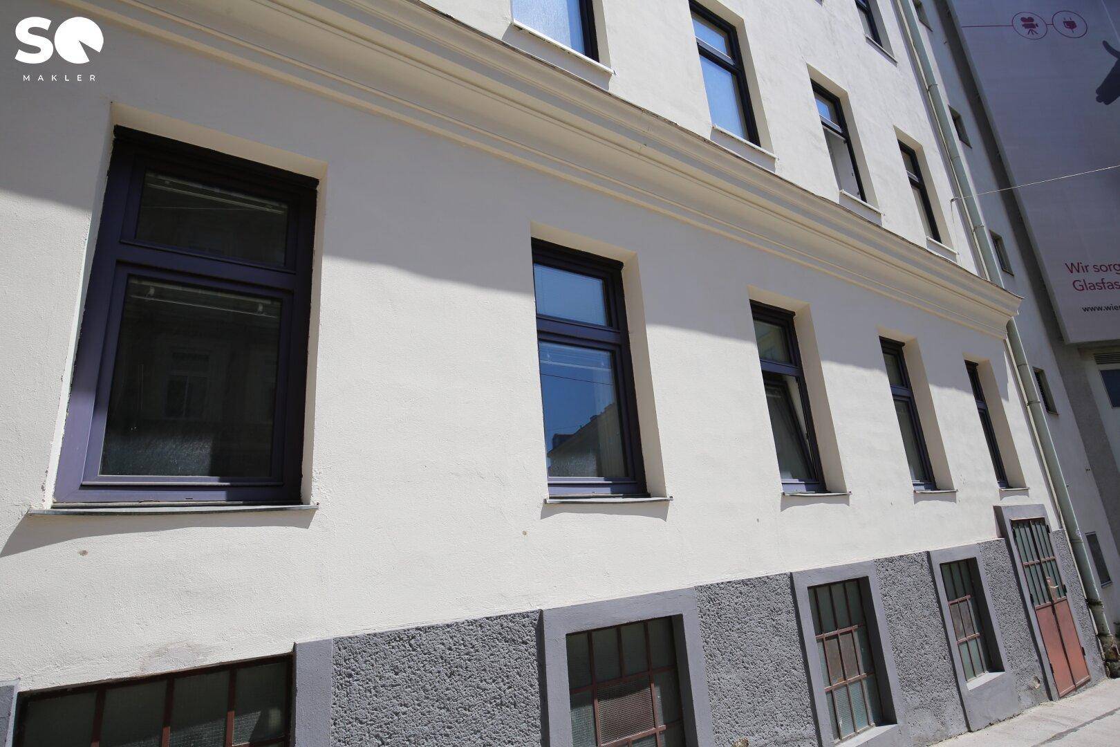Nahaufnahme der weißen Fassade eines Gebäudes mit dunklen Fenstern und grauen Sockel.