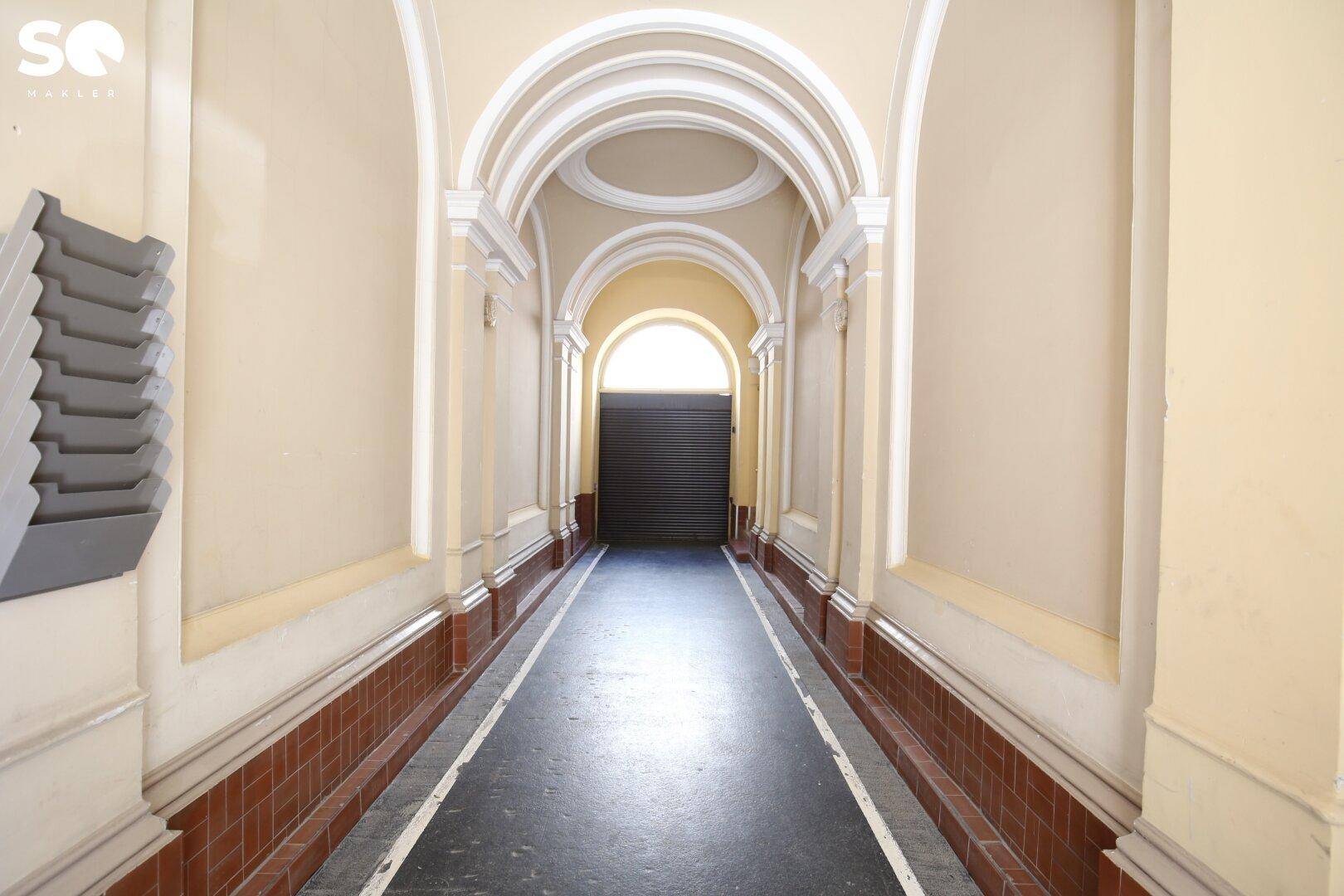 Historischer Eingangsbereich mit Bögen und dekorativen Elementen, der zu einem geschlossenen Tor führt.
