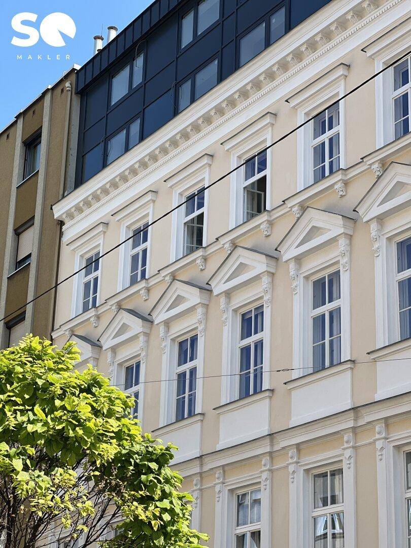 Historische Fassade mit verzierten Fenstern und einem modernen Dachaufbau unter blauem Himmel.