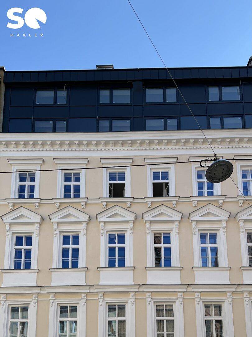 Detailansicht der historischen Fassade mit modernem Dachgeschoss und blauen Fenstern.