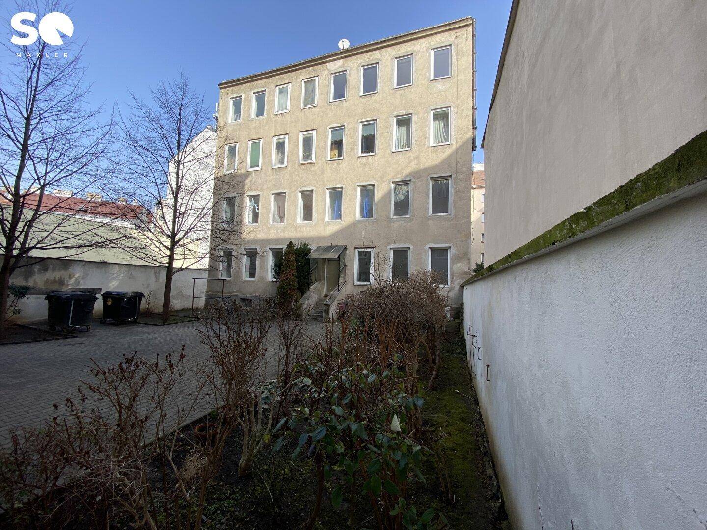 Gebäudefassade eines Mehrfamilienhauses von einem Hinterhof aus gesehen mit kahlen Bäumen.
